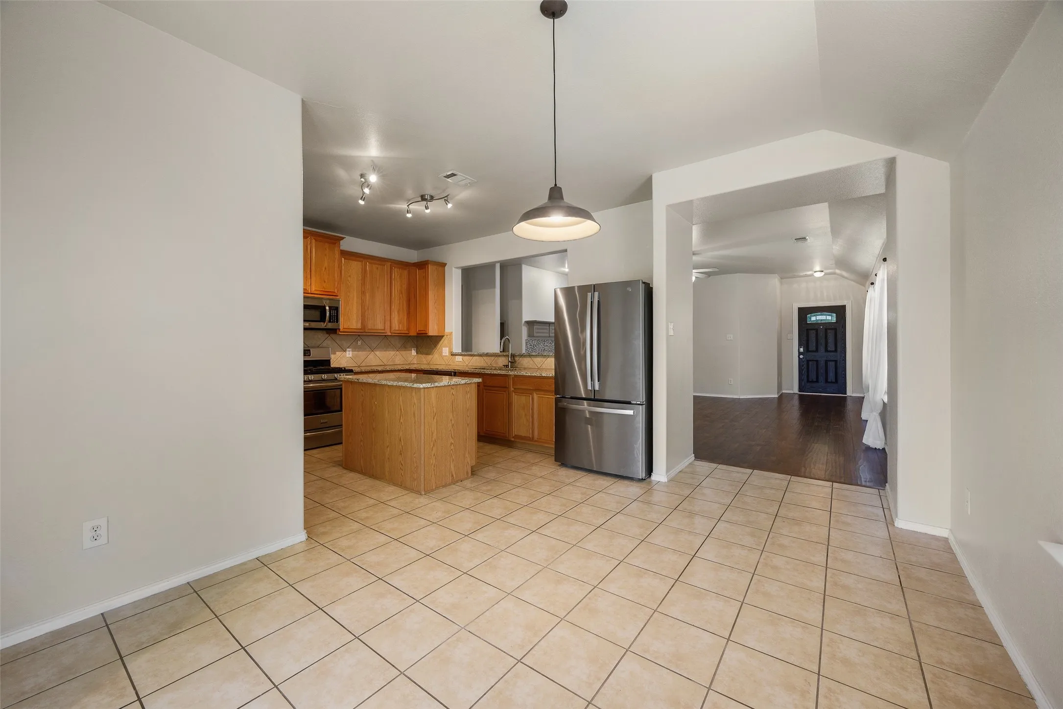 Kitchen featuring wood cabinetry, stainless steel appliances, a center island with a stone-finish countertop, and tile flooring