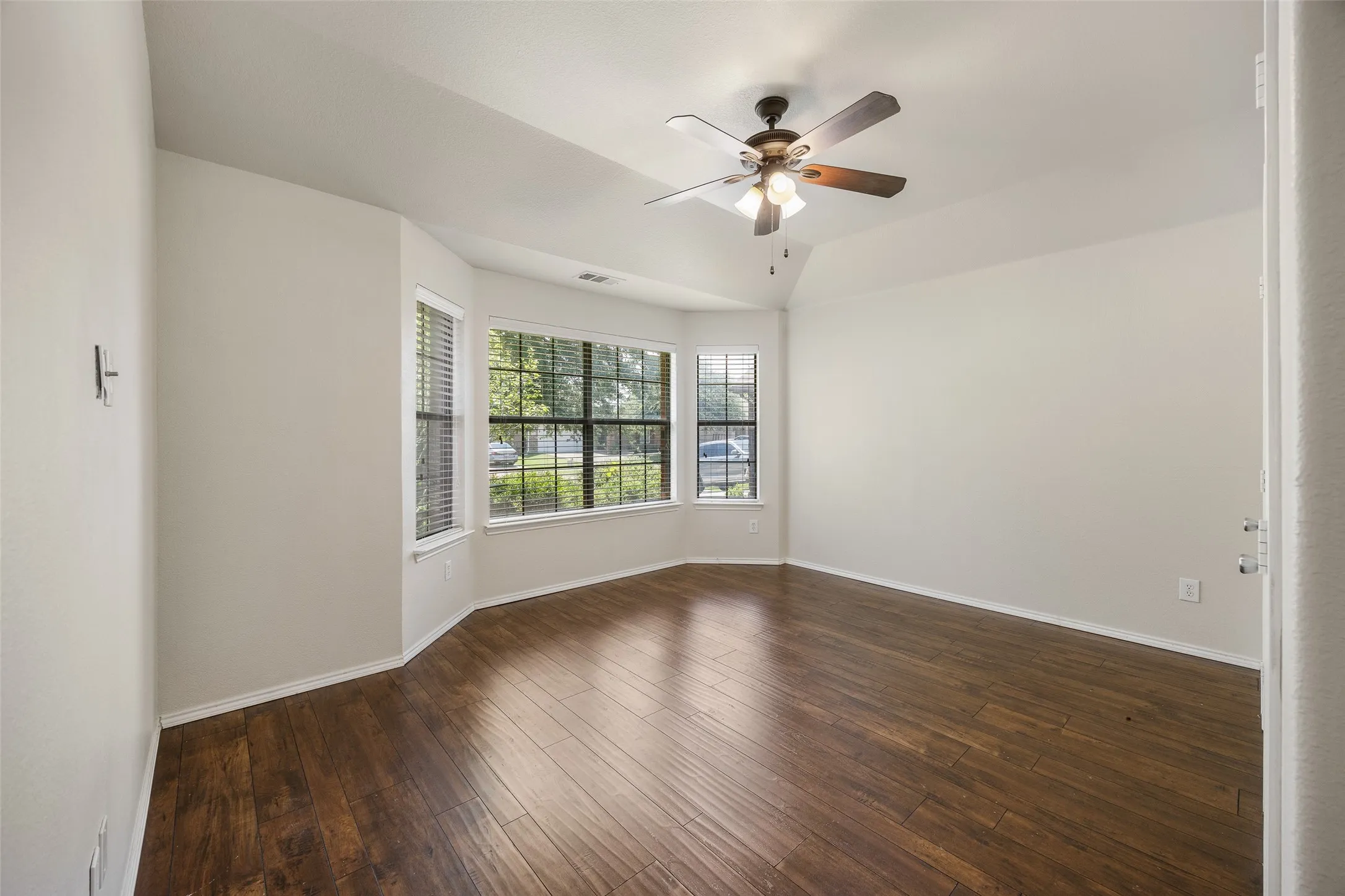 Spacious interior room featuring wood-finish flooring, vaulted ceiling, and a ceiling fan with integrated lighting
