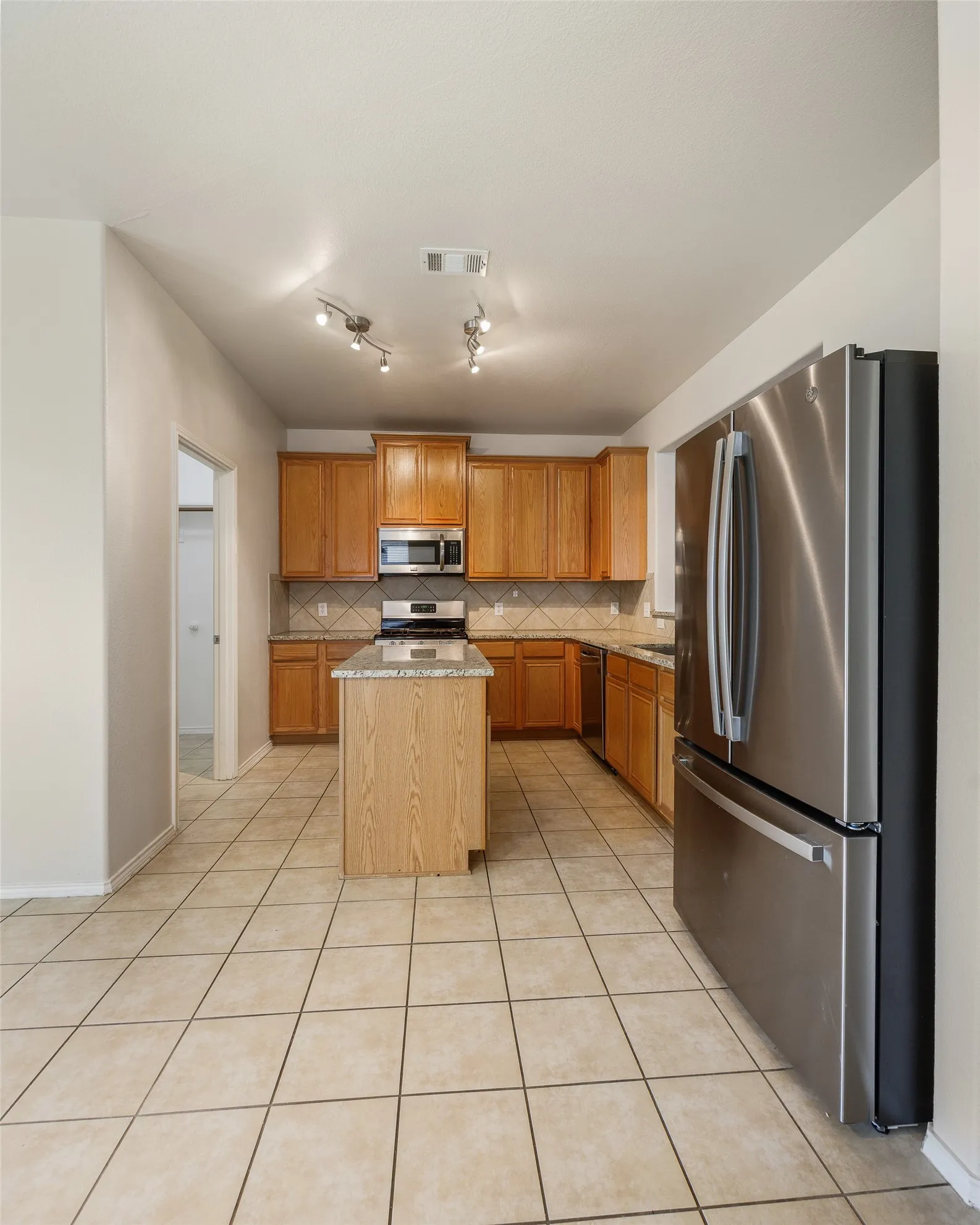 Kitchen featuring a central island with granite countertop, wood cabinetry, stainless steel appliances, and tile flooring
