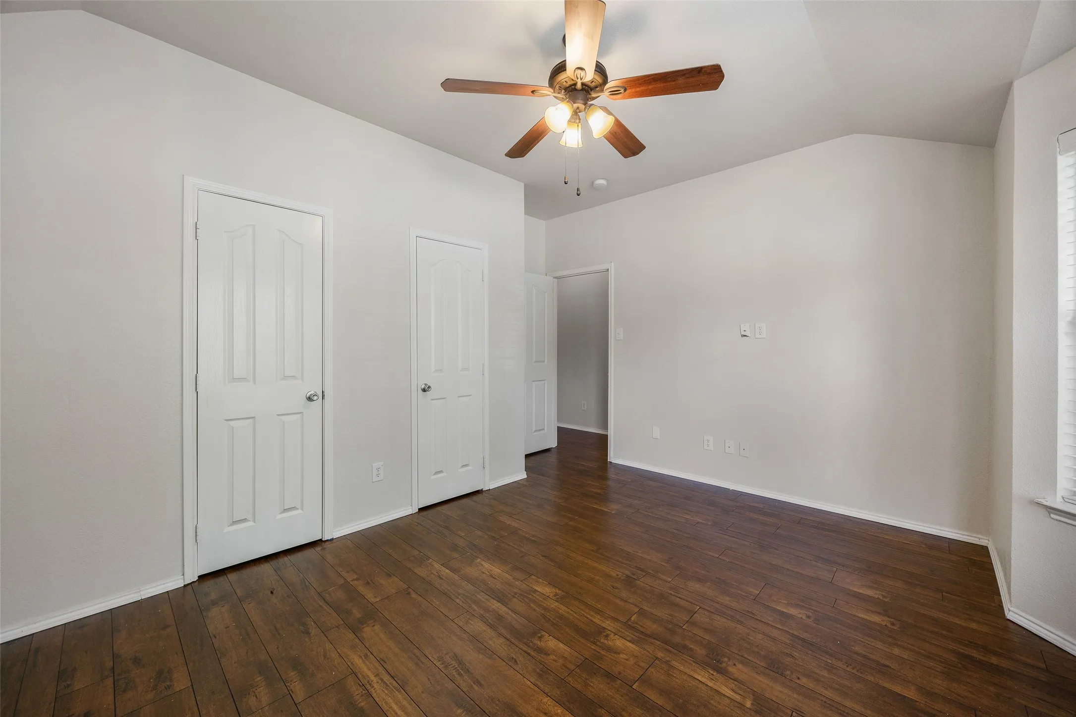 Spacious interior featuring rich wood-finish flooring, a ceiling fan with light fixture, white interior doors, and clean white walls
