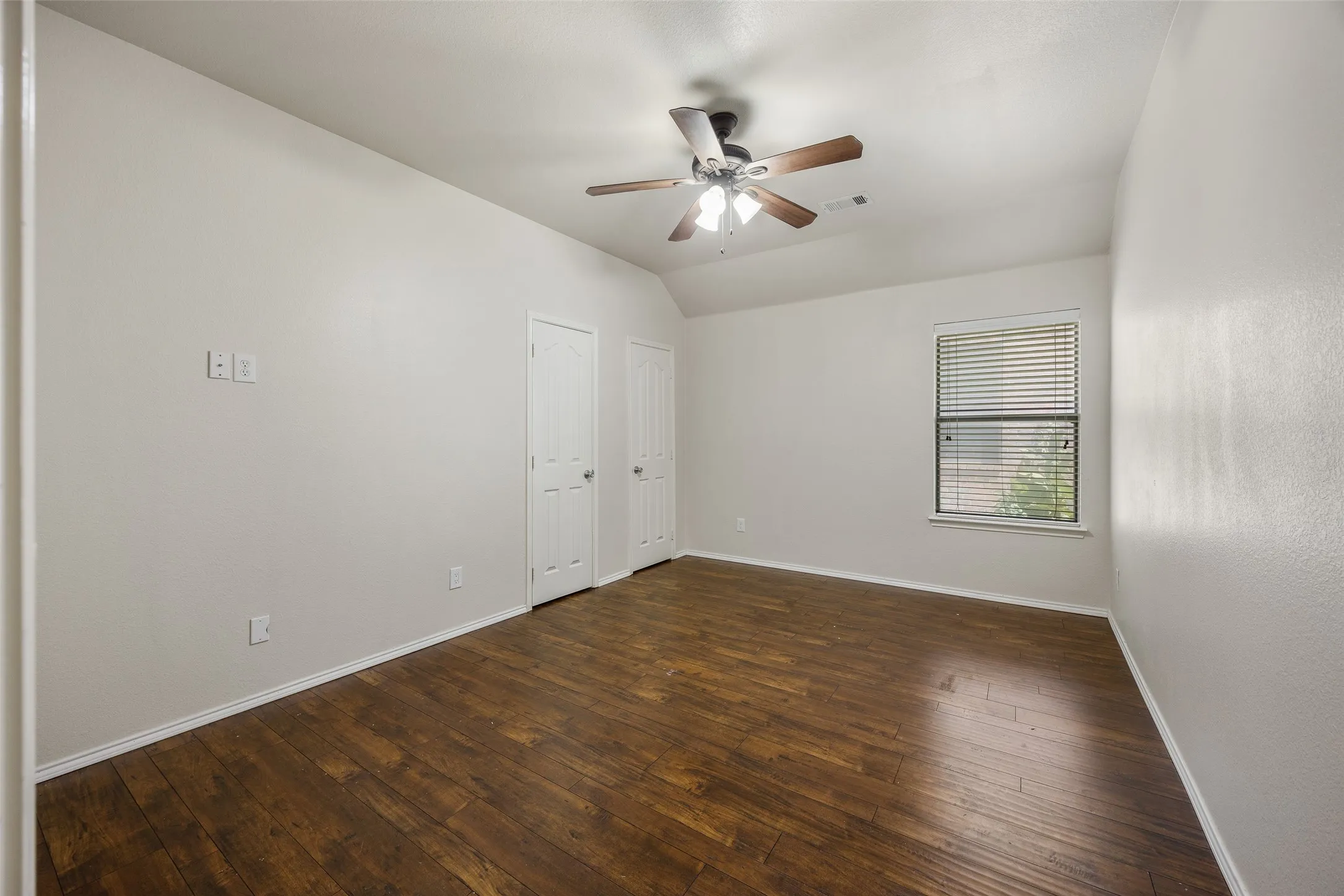 Room featuring wood-finish flooring, a ceiling fan with integrated lighting, and two panel doors