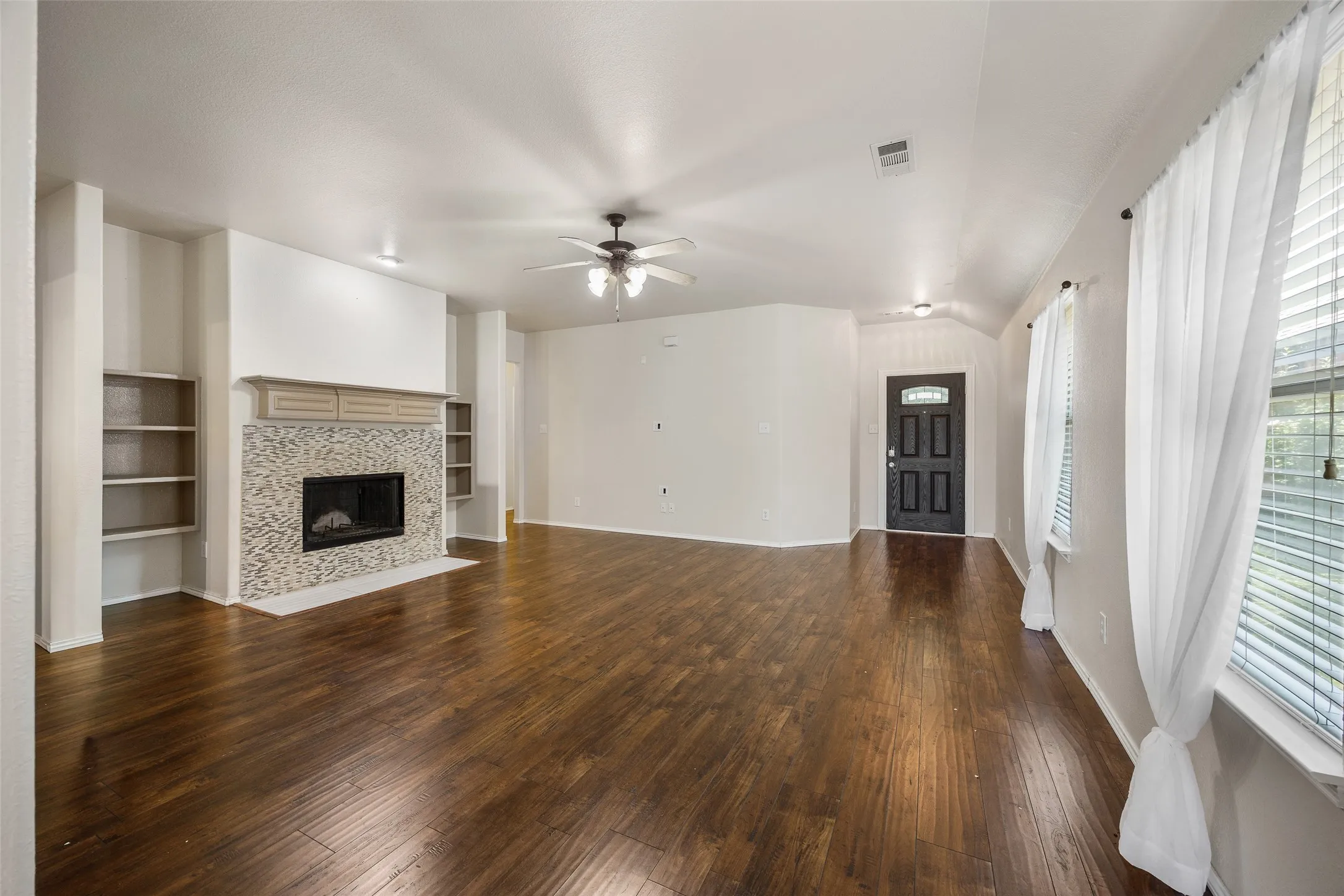 Spacious living area featuring wood-finish flooring, a fireplace with a mosaic tile surround and decorative mantel, and built-in shelving