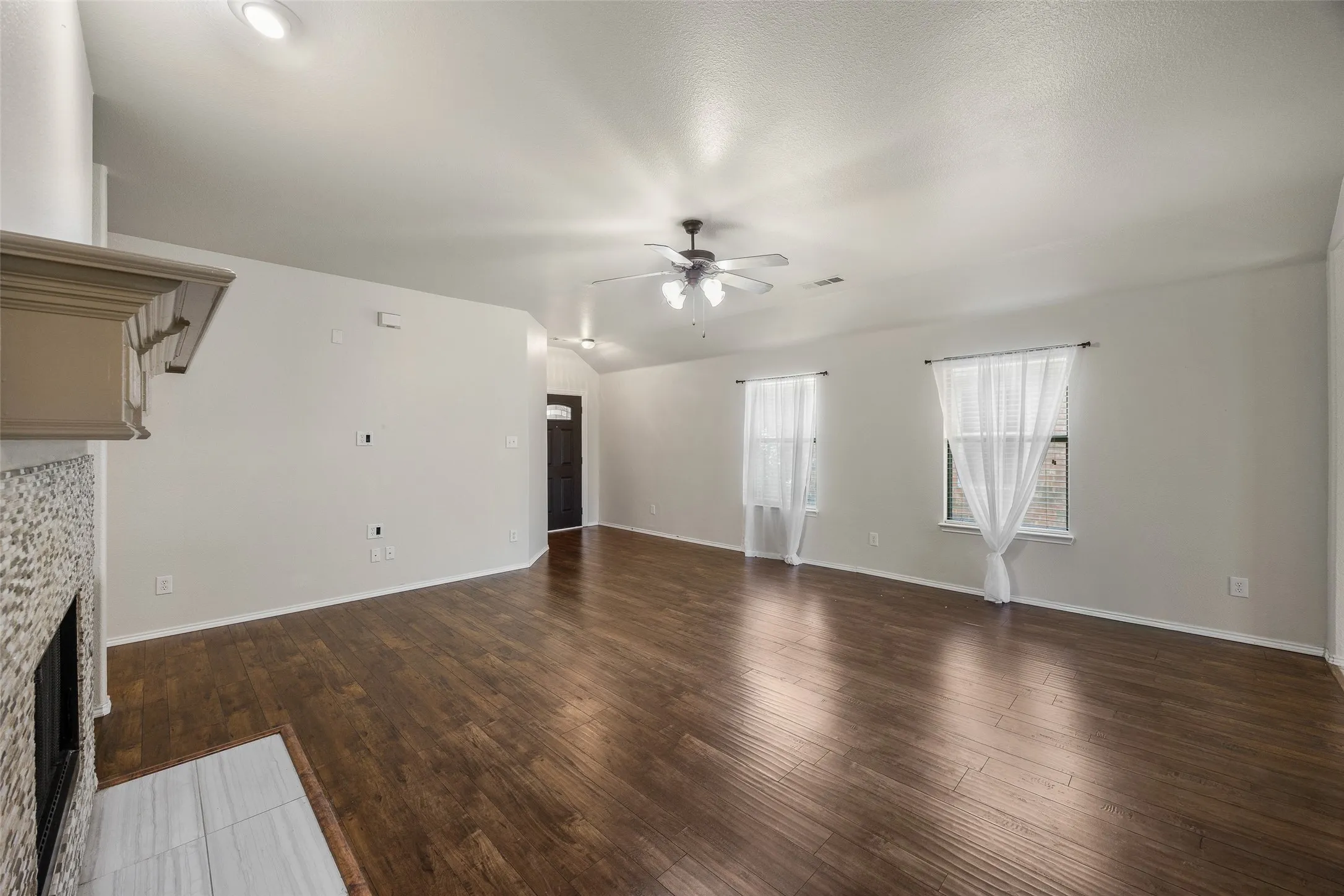 Spacious living area featuring wood-finish flooring, vaulted ceilings, recessed lighting, and a fireplace with a decorative mantel and mosaic tile surround