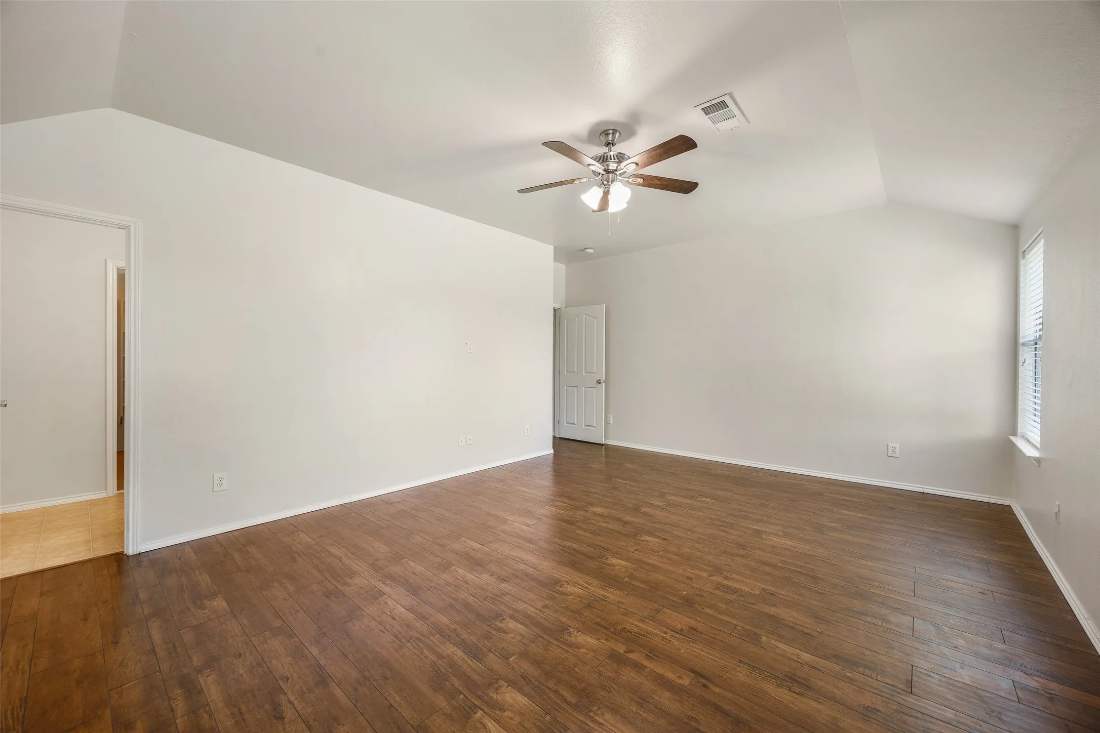 Spacious room featuring wood-finish flooring, vaulted ceilings, and a ceiling fan
