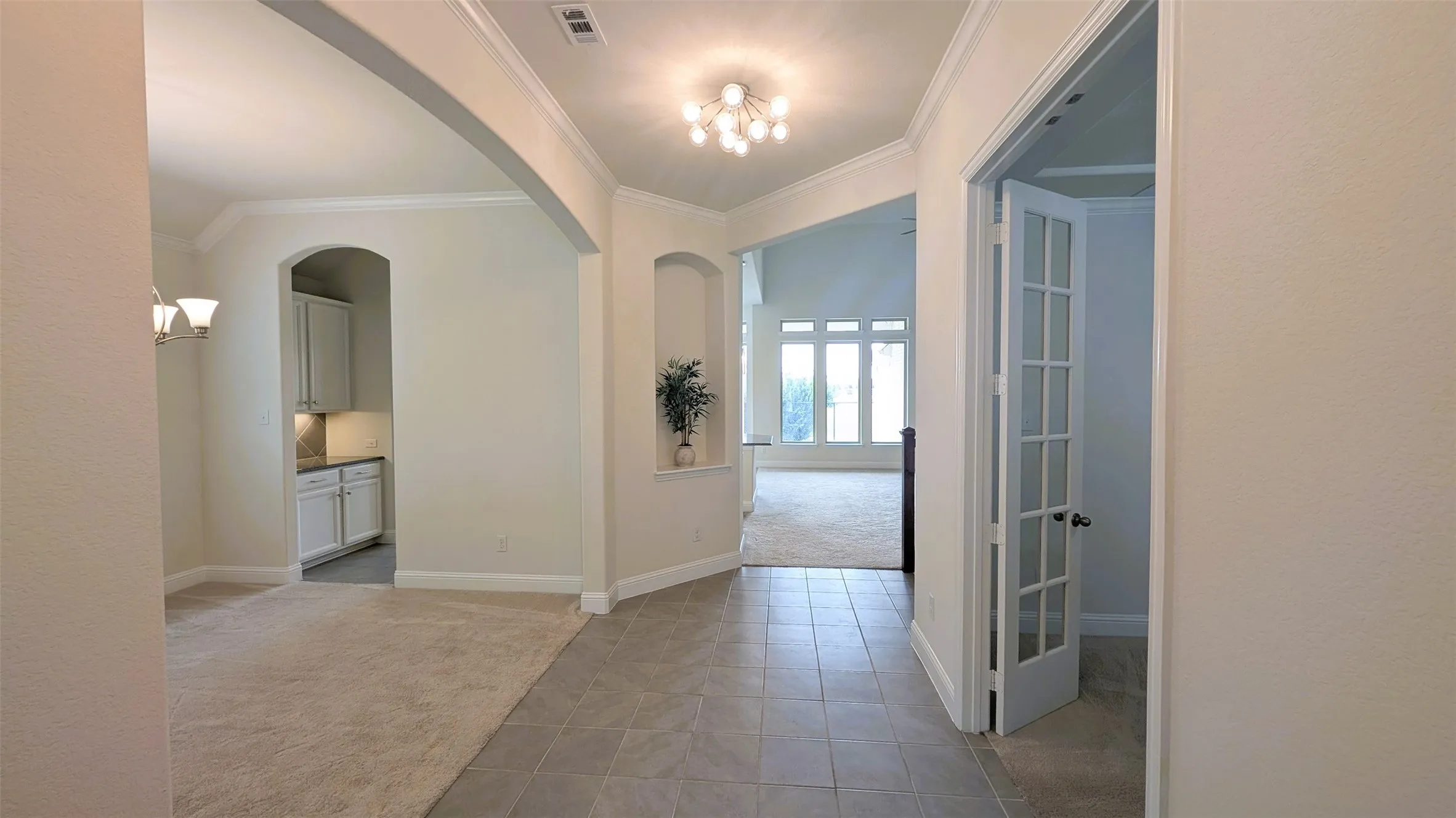 Entry foyer with tile flooring leading to an arched hallway, an open living area with large windows, and a room featuring French doors