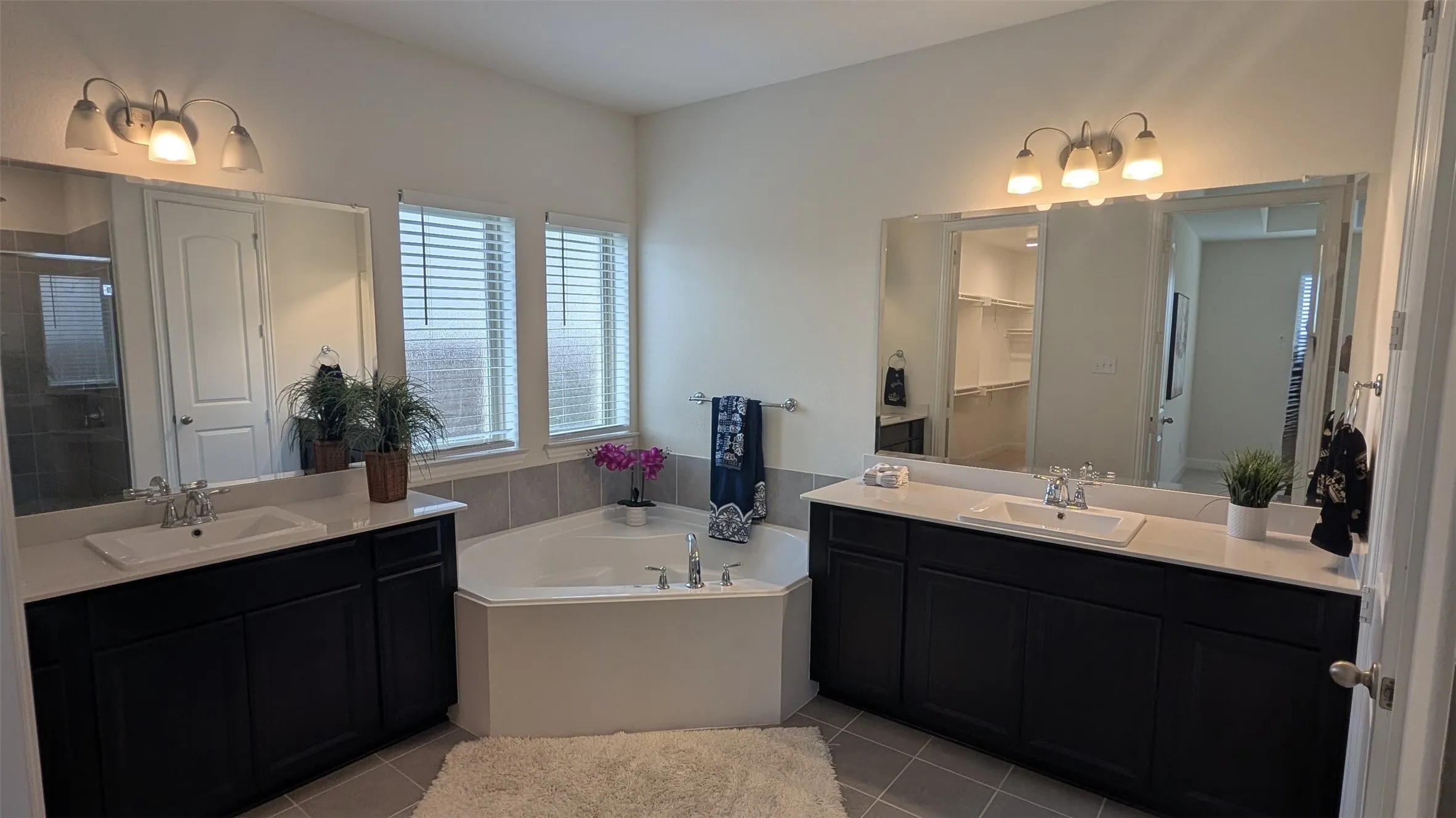Spacious bathroom featuring a corner soaking tub, dual vanities with white countertops, expansive mirrors, and natural light from multiple windows