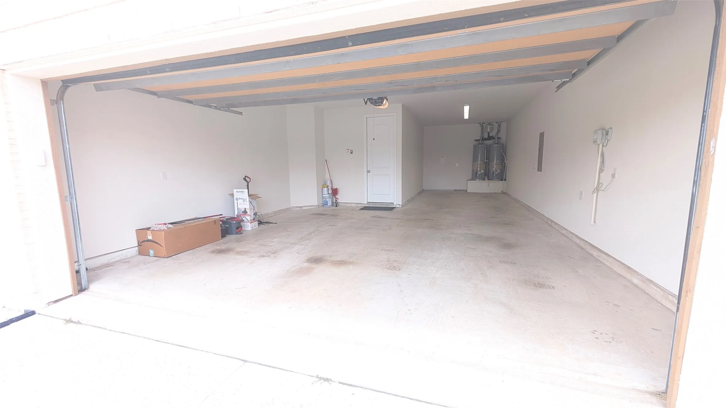 Spacious two-car garage with an overhead automatic door, concrete flooring, interior access door, and wall-mounted lighting