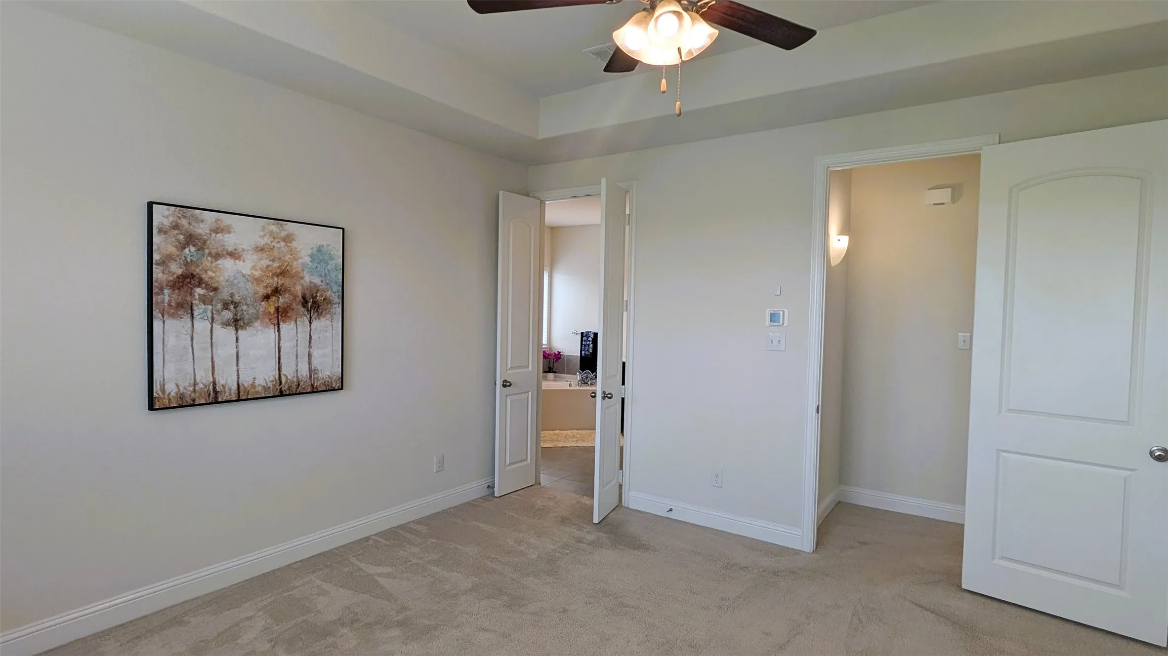 Plush carpeting throughout the room, tray ceiling with a ceiling fan and light fixture, multiple white panel doors, and neutral wall tones
