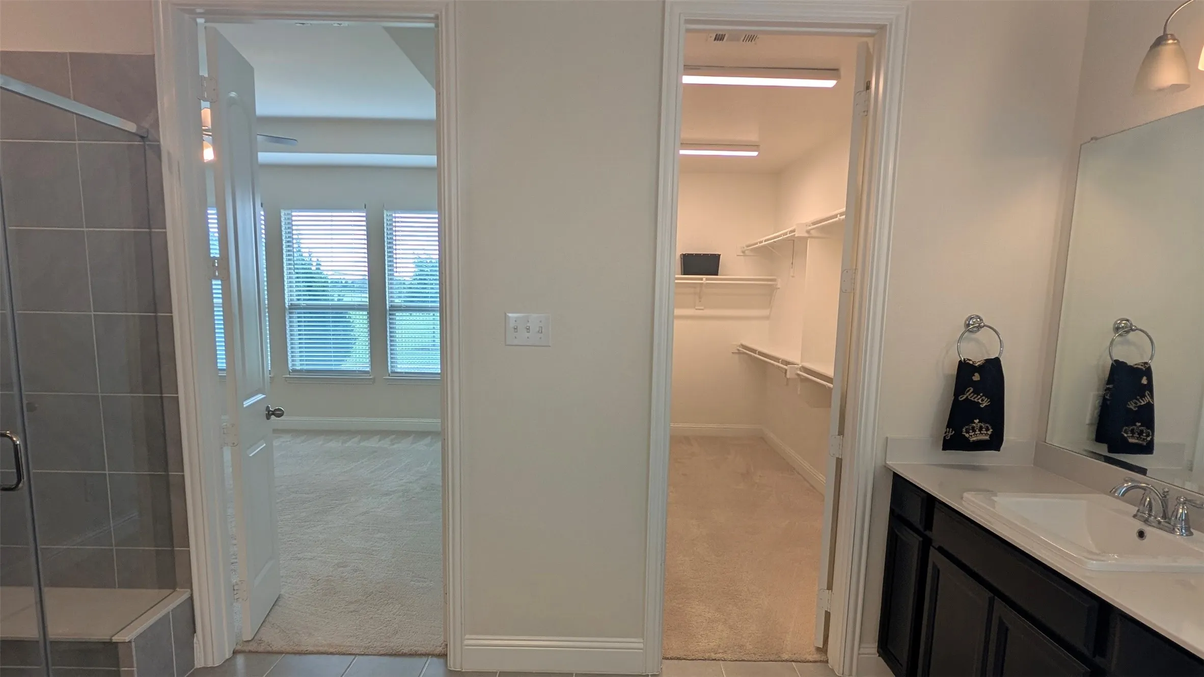 Bathroom featuring a walk-in shower with tiled walls and an integrated bench, a vanity with a dark wood-finish cabinet and a white countertop with an undermount sink, a large wall-mounted mirror, and a spacious walk-in closet with built-in shelving and hanging rods