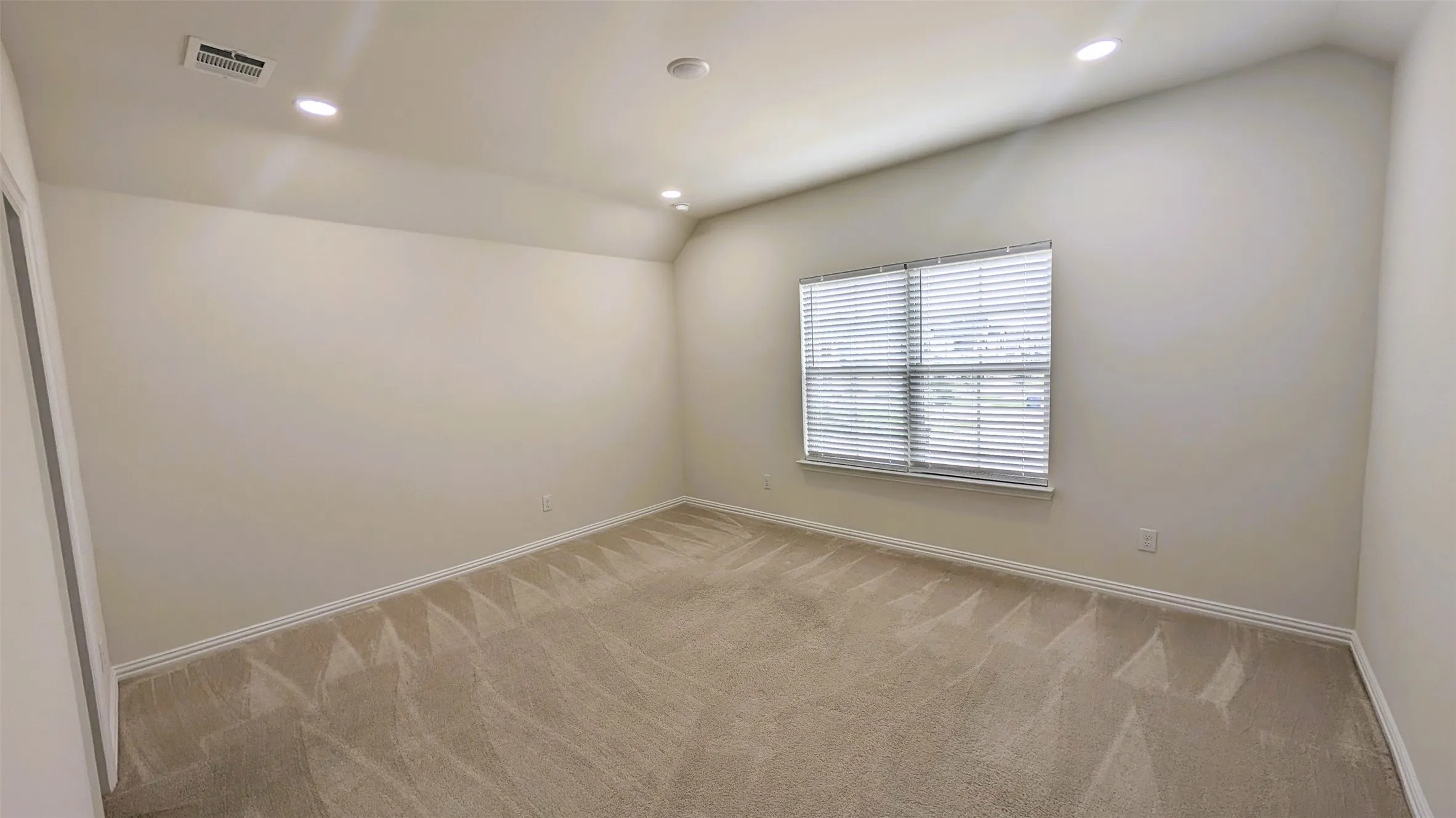 Carpeted interior space featuring neutral wall tones, a vaulted ceiling, recessed lighting, and a window with horizontal blinds