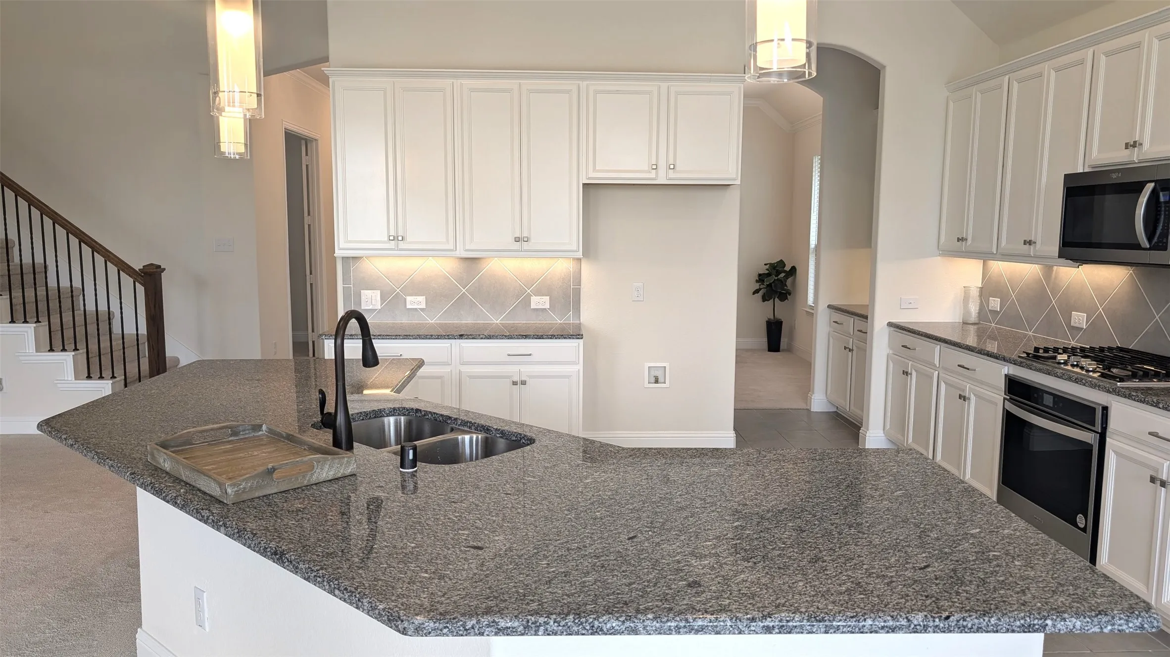 Spacious kitchen featuring an expansive island with a double sink, white cabinetry, under-cabinet lighting, a diagonal tile backsplash, and stainless steel appliances