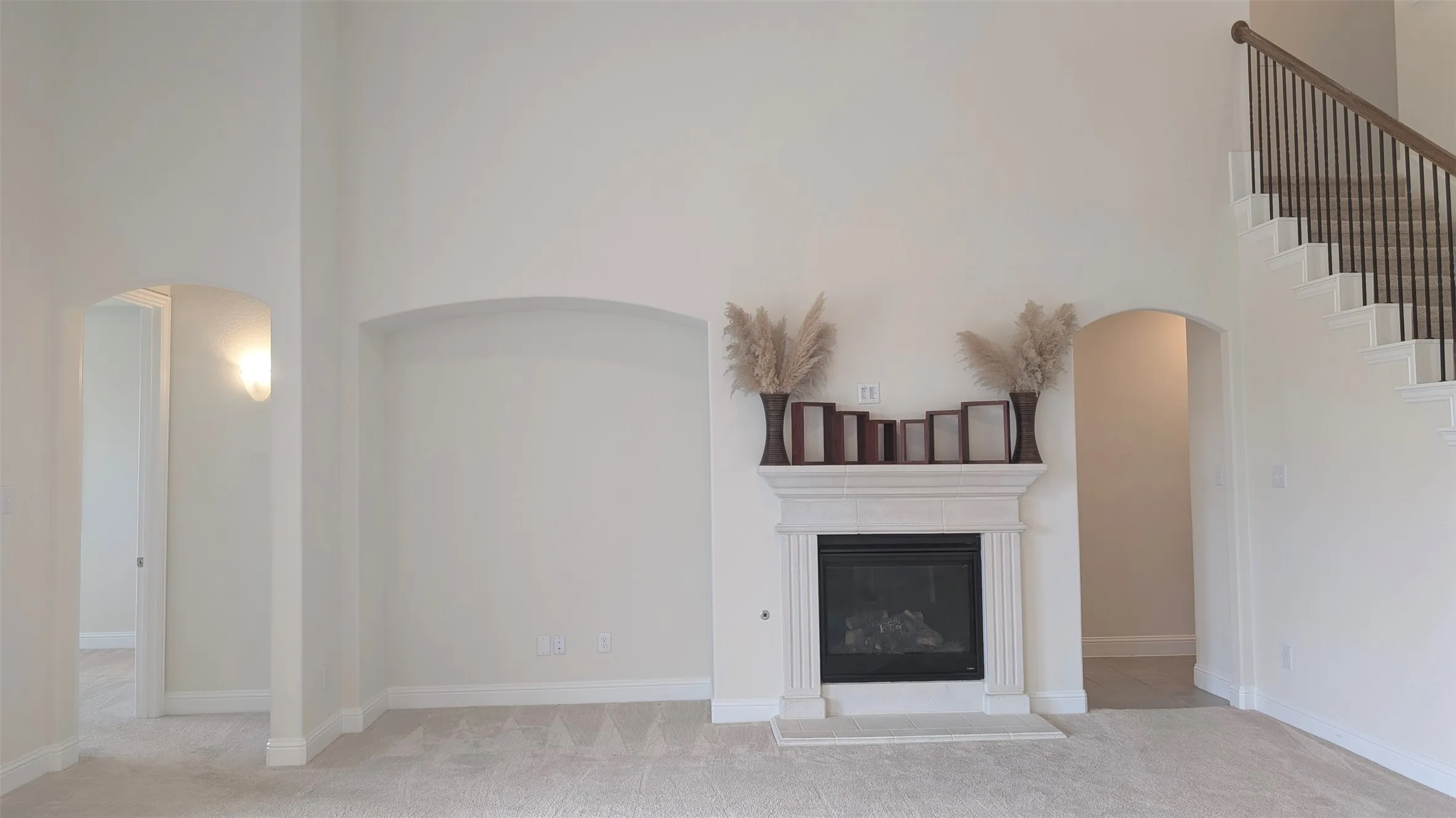 Spacious living area featuring a stone fireplace with mantel, high ceilings, arched doorways, and a carpeted staircase with wrought iron balusters