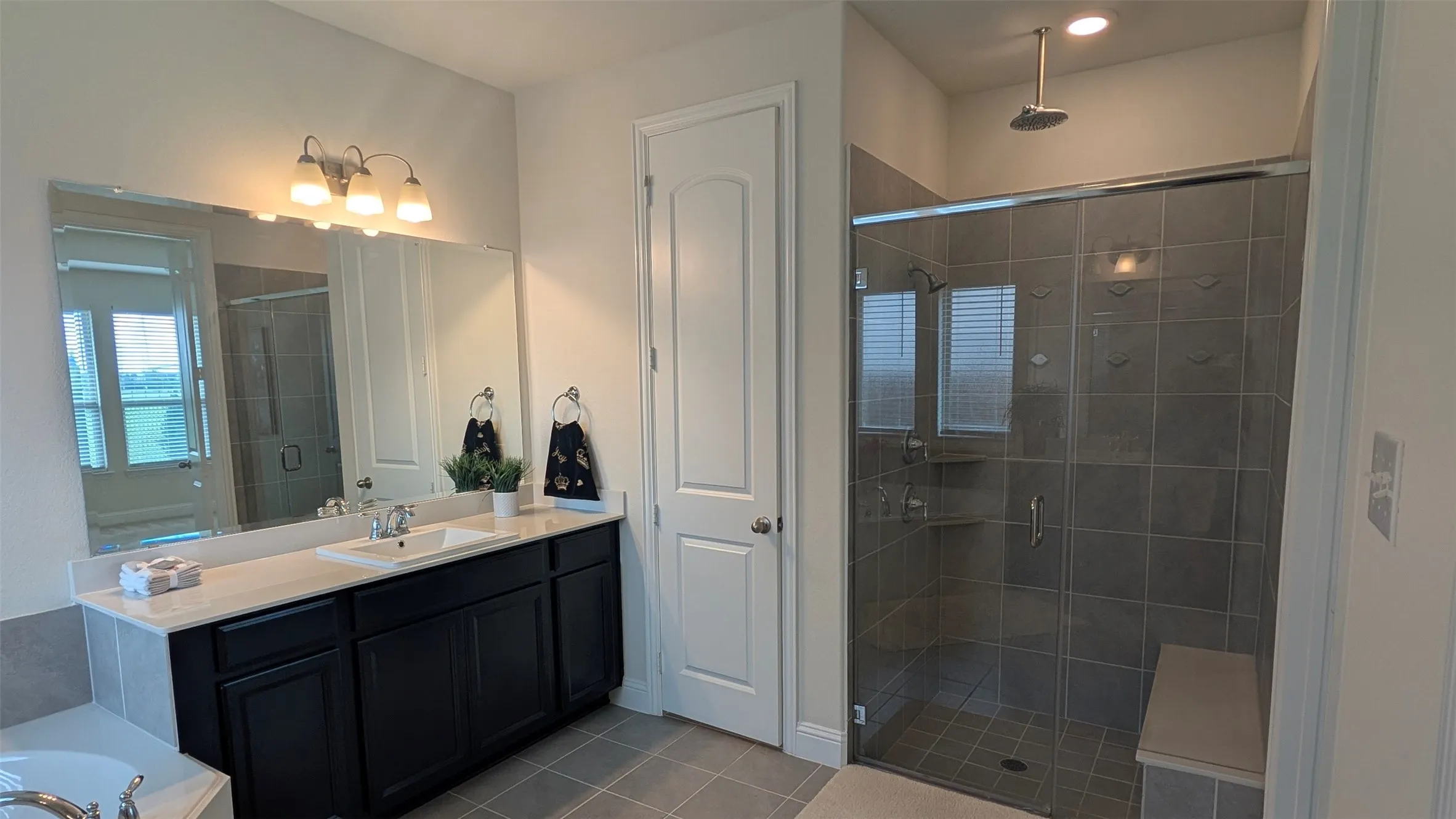 Bathroom featuring a double vanity with dark cabinetry, integrated sink, and expansive mirror