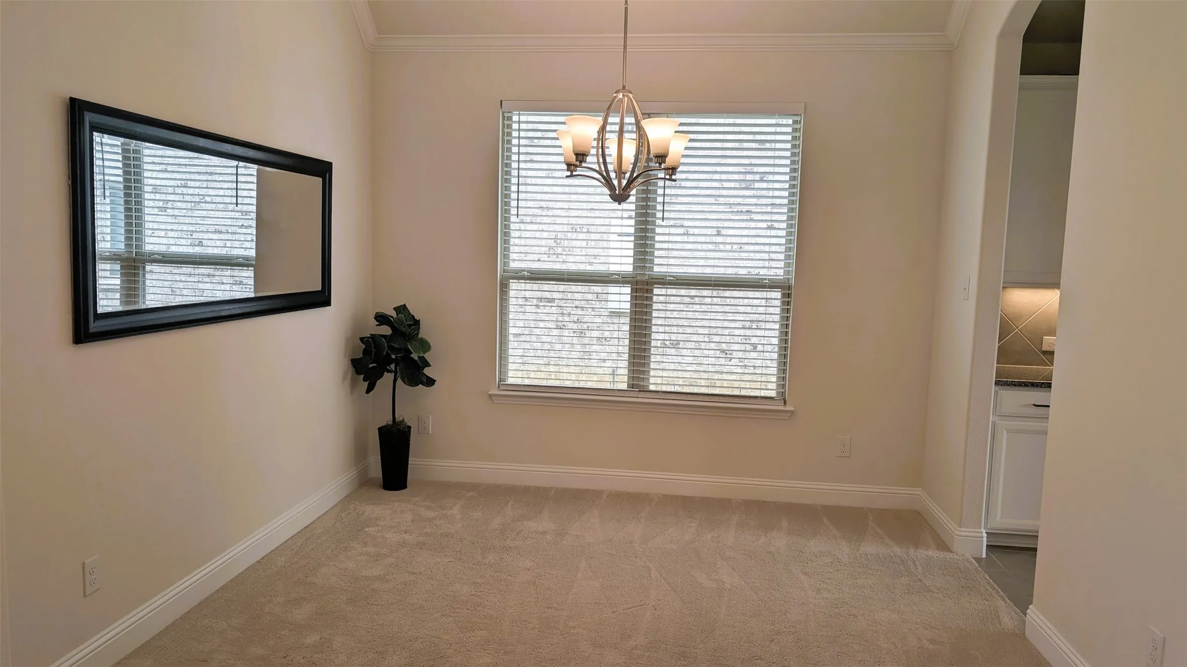 Spacious room featuring neutral carpeting, a large window with blinds, and an overhead chandelier light fixture