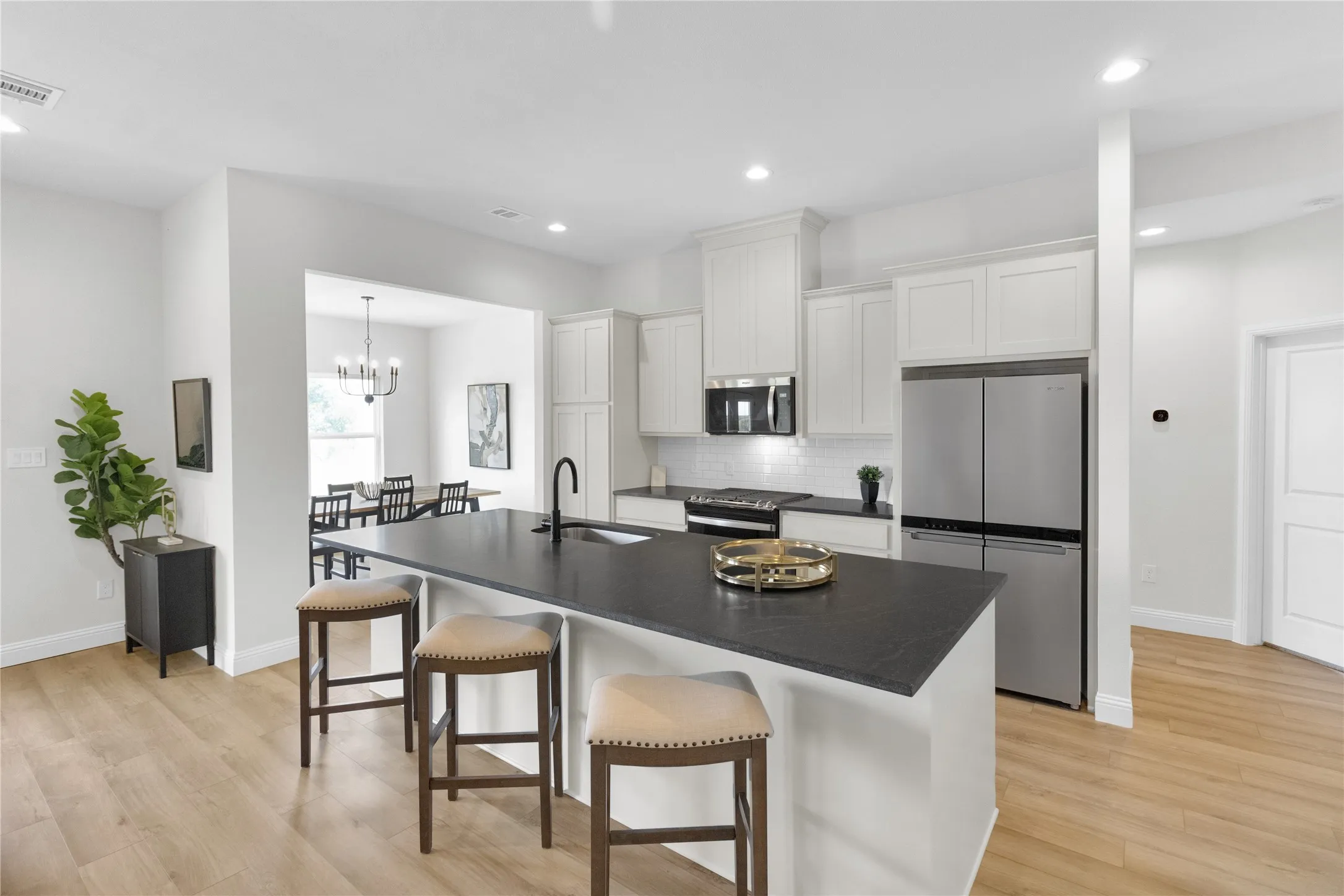 Kitchen featuring a large island with dark countertops, white cabinetry, stainless steel appliances, a white subway tile backsplash, and light wood-finish flooring