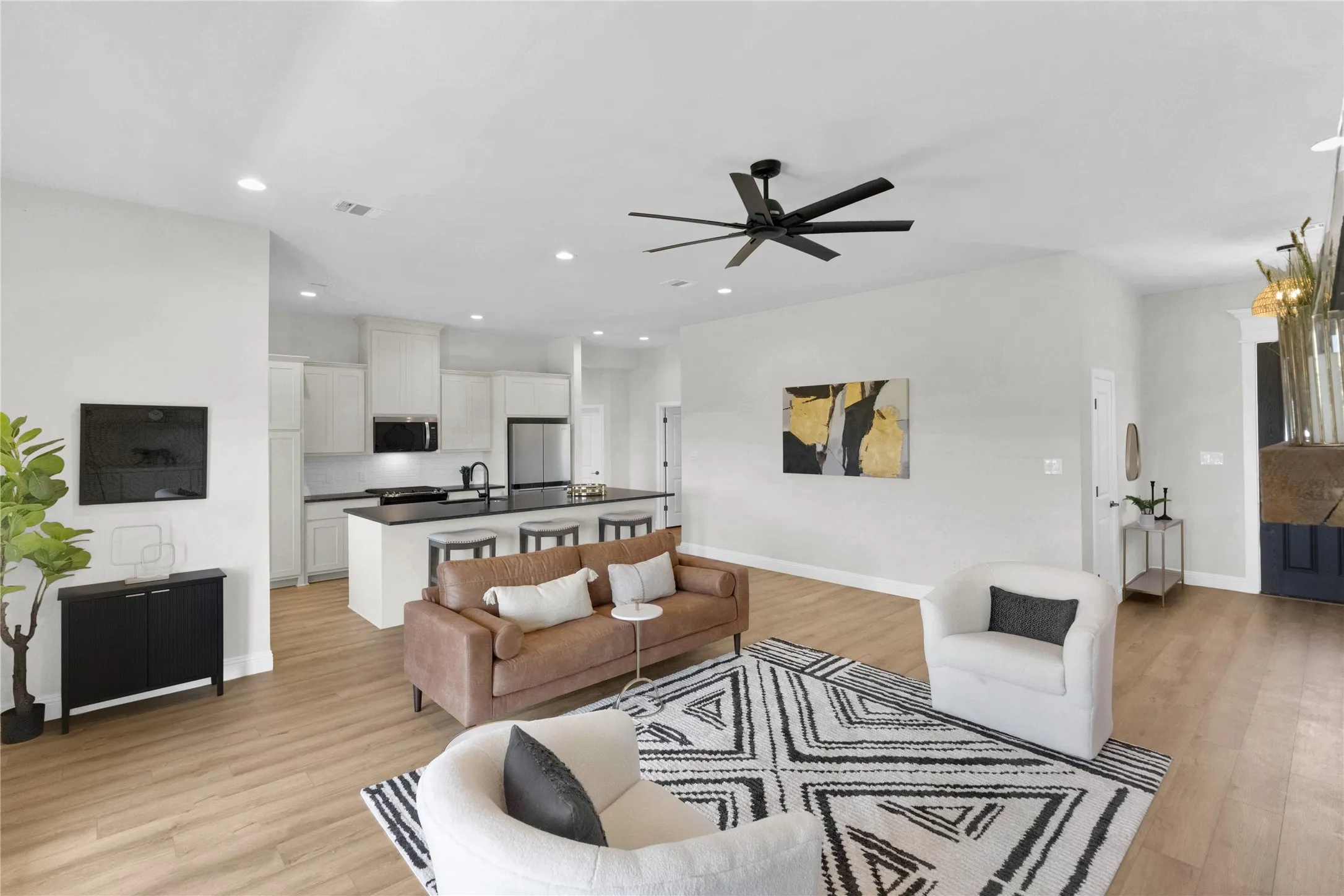Expansive open-concept living area featuring wood-finish flooring, a contemporary ceiling fan, recessed lighting, and a kitchen with an island, white cabinetry, and stainless steel appliances