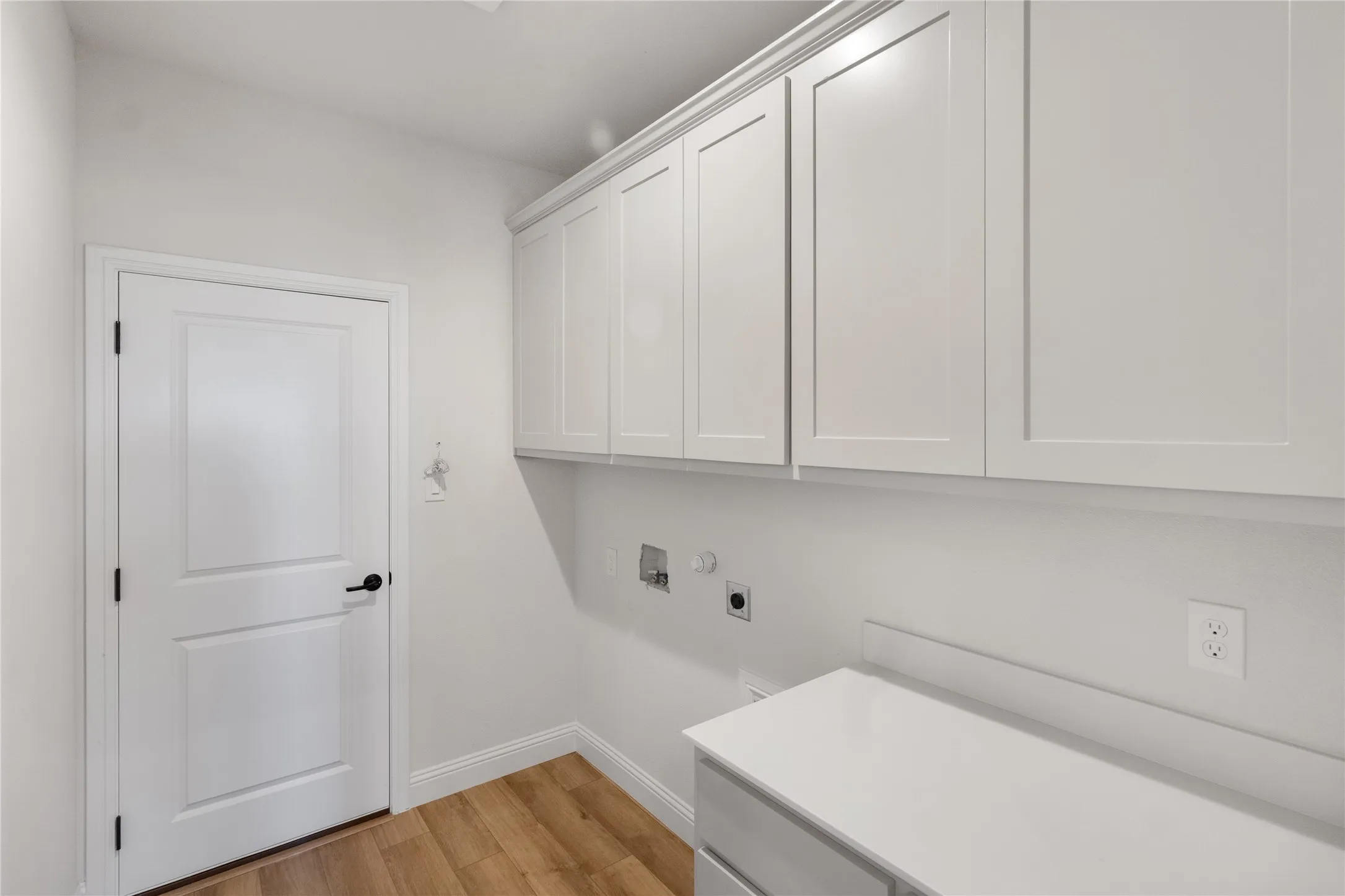 Laundry room featuring wood-finish flooring, white shaker cabinetry, white countertop, and white walls