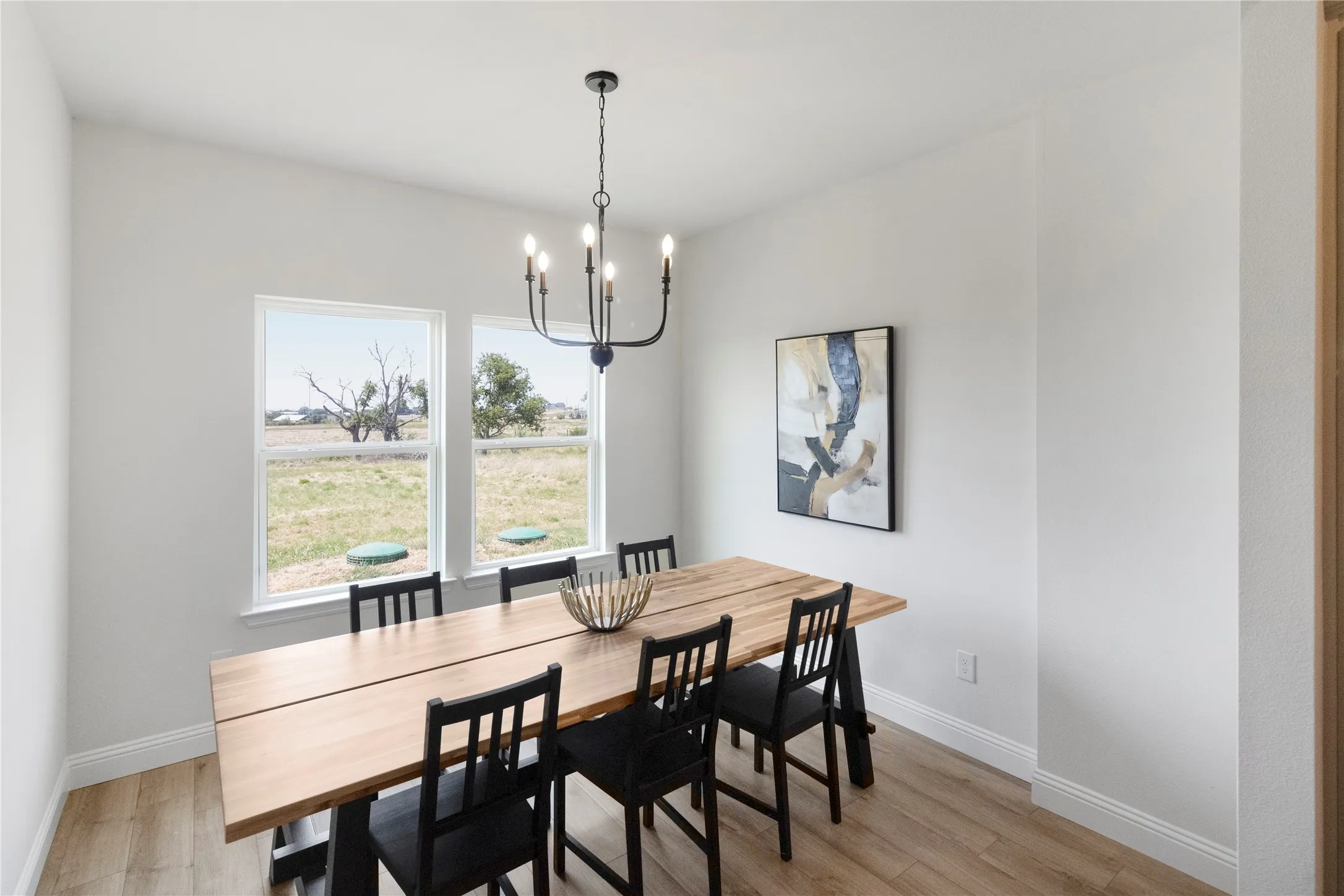 Bright interior room featuring wood-finish flooring, white walls, and a black ceiling-mounted chandelier