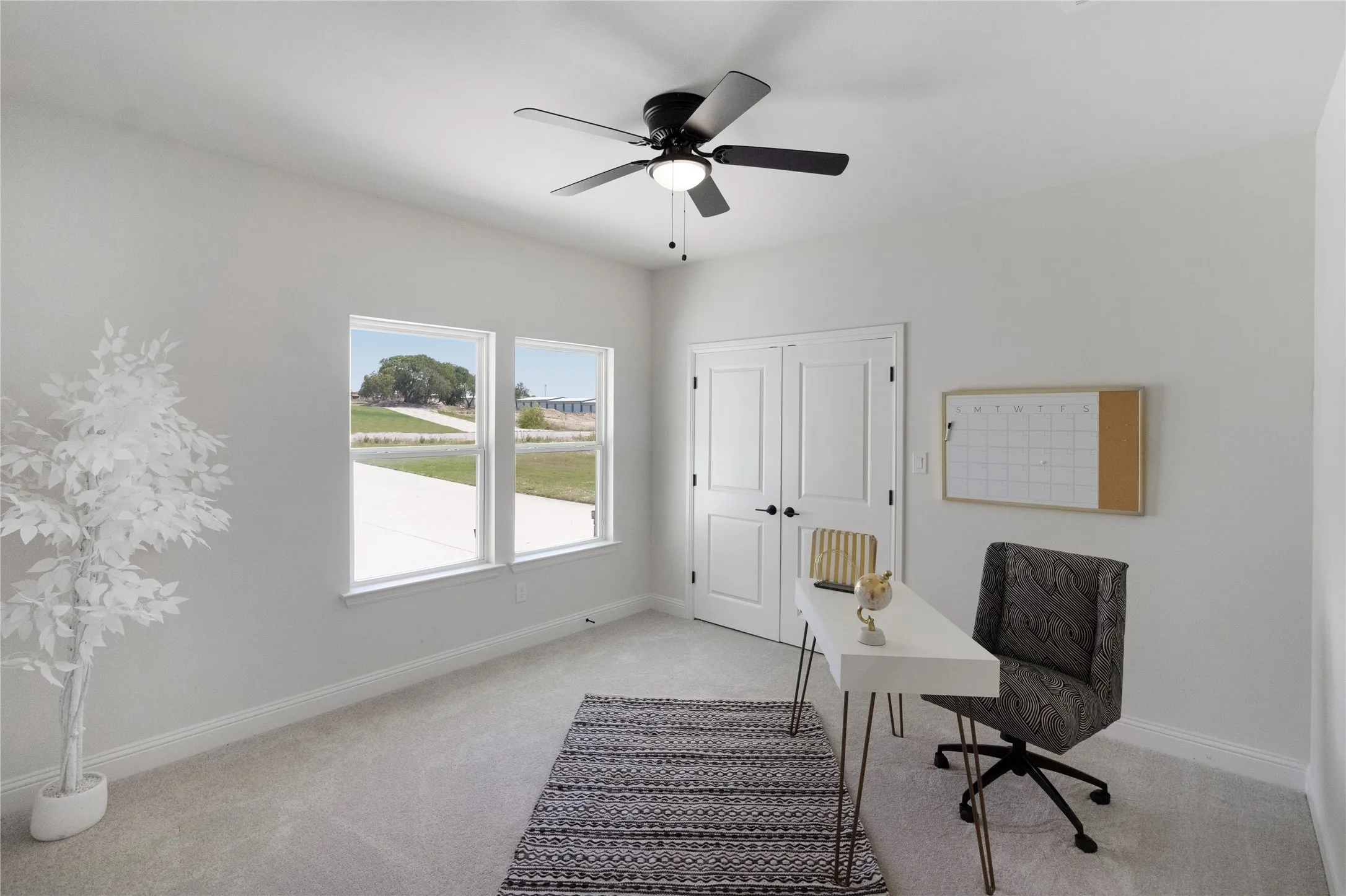 Light-filled room featuring two large windows, soft gray carpeting, and a ceiling fan with integrated lighting