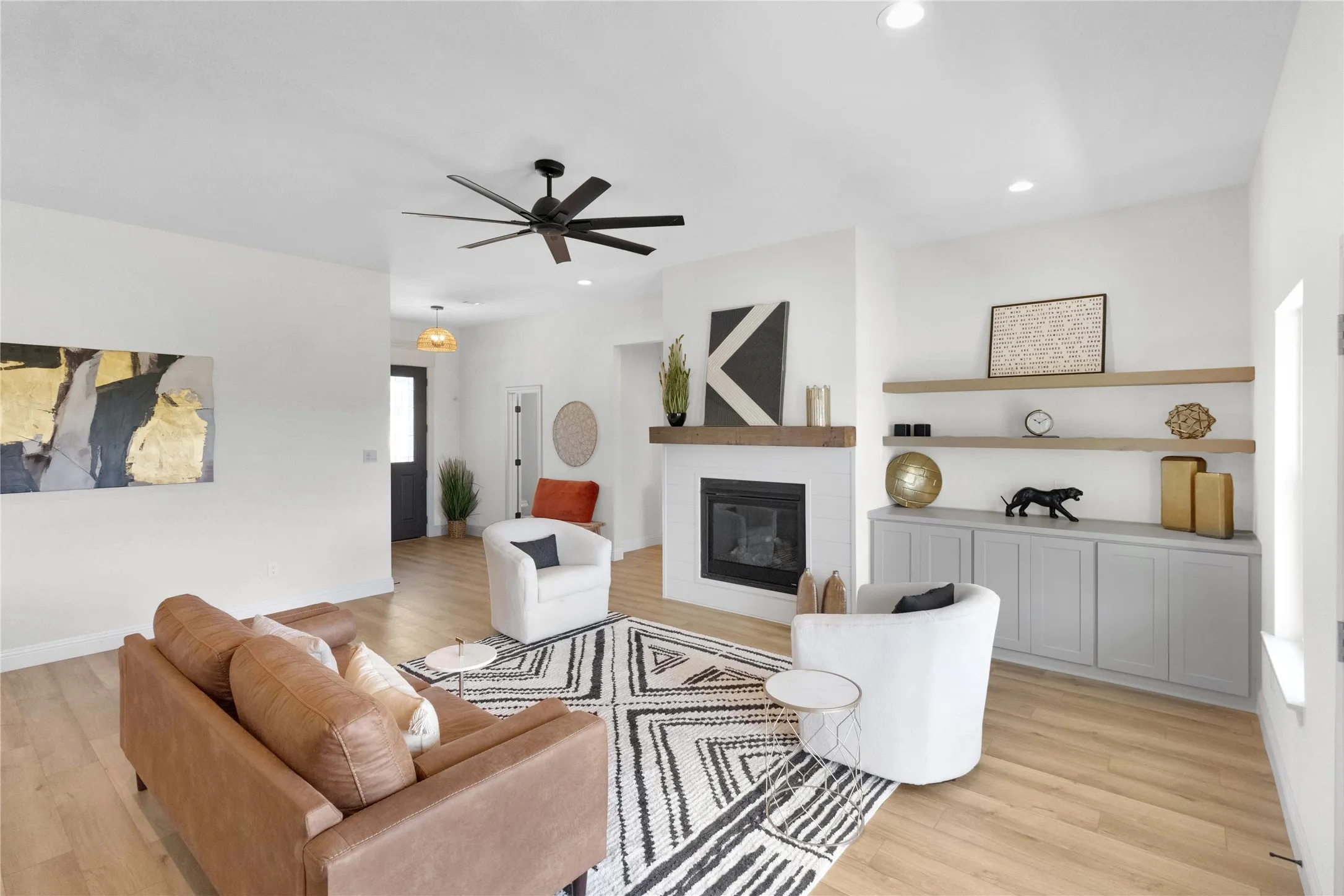Living area featuring light wood-finish flooring, a white brick fireplace with a wood mantle, a built-in media console with light gray cabinetry, and recessed lighting