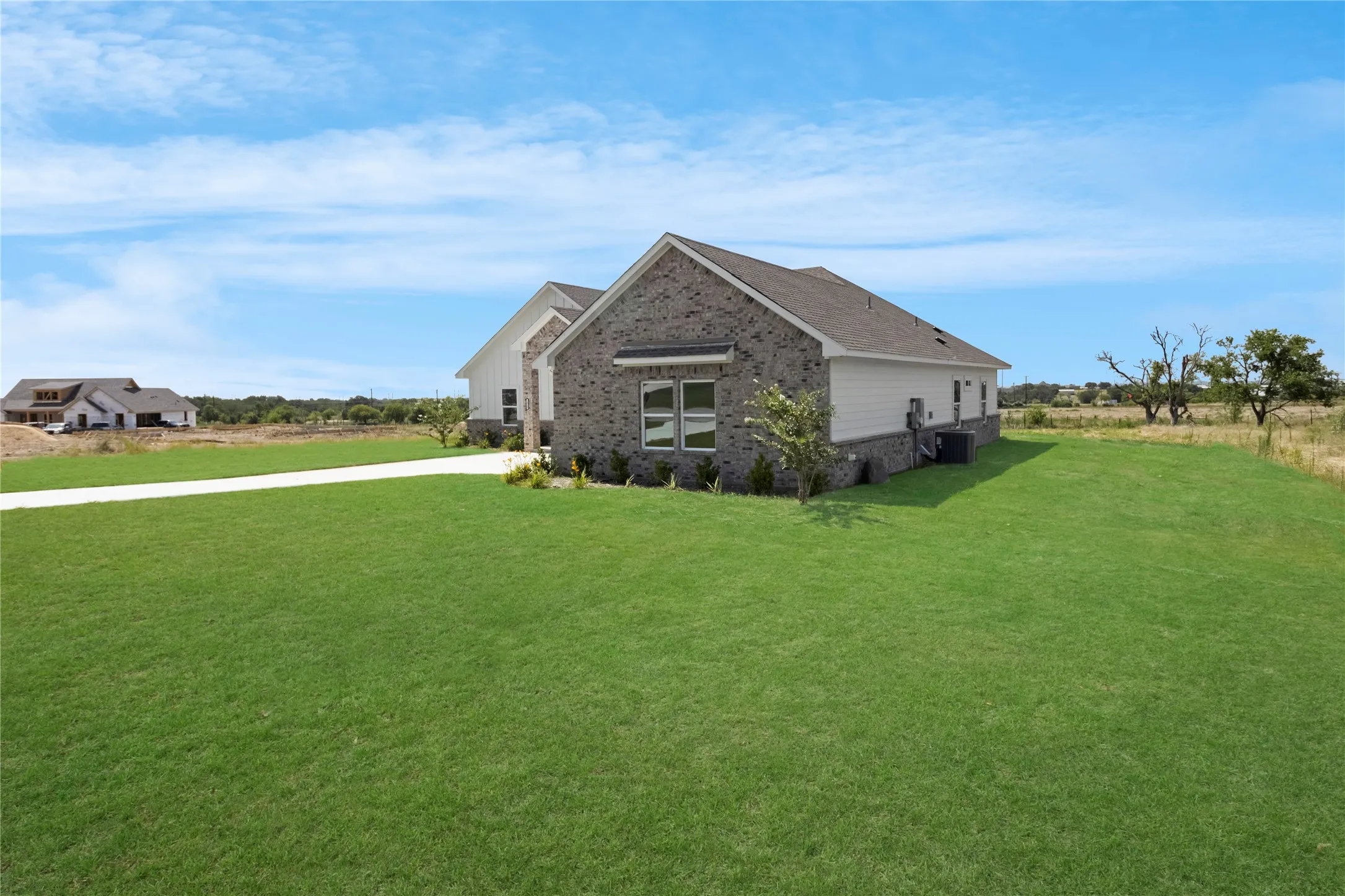 Expansive green lawn surrounding a residence featuring a brick and white siding exterior with a dark shingle roof