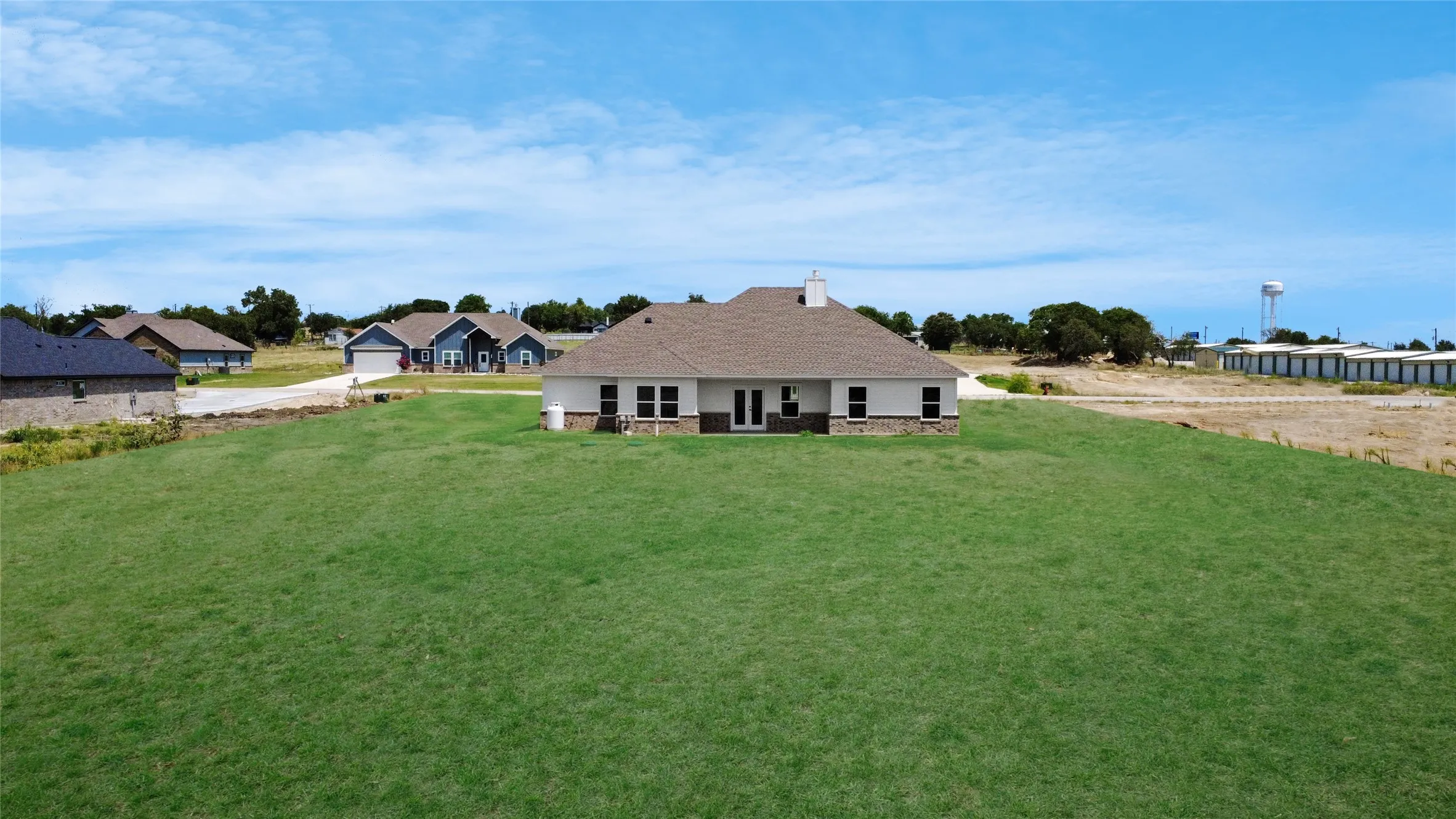 Expansive green lawn surrounds a single-story residence featuring white siding and a stone-accented foundation