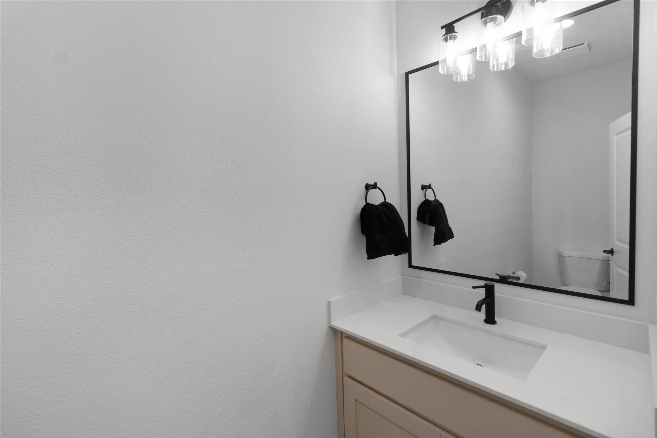 Bathroom vanity featuring a rectangular undermount sink, light-toned countertop, and matte black faucet