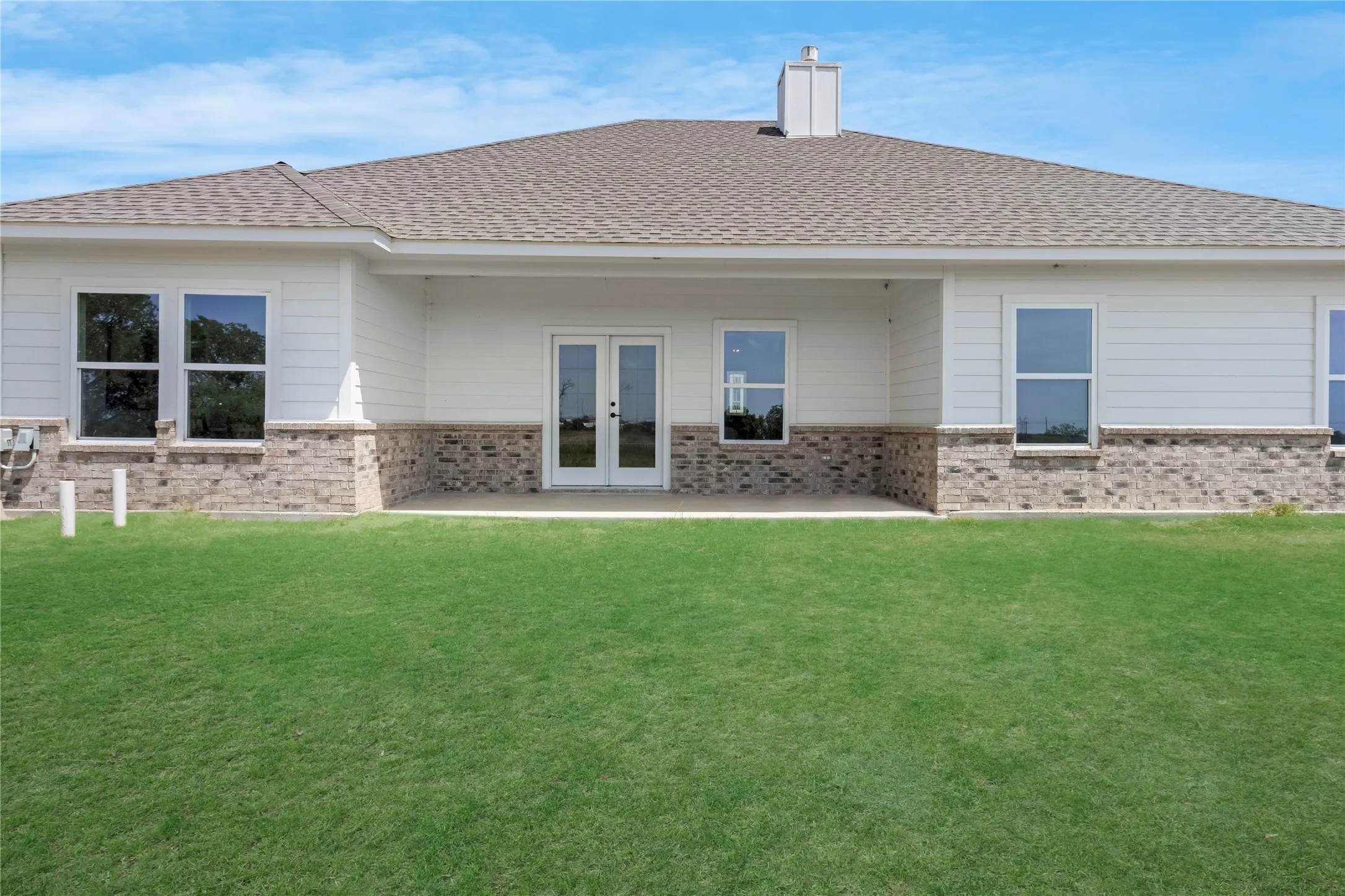 Rear exterior featuring a covered patio, double glass doors, multiple large windows, a shingled roof, and a stone and siding facade