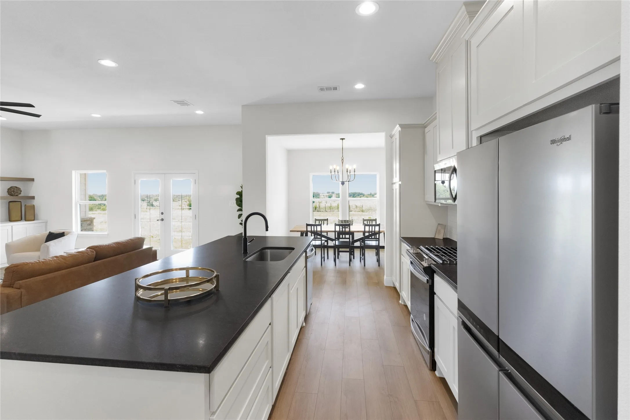 Modern kitchen featuring an extended island with a built-in sink and matte black faucet, stainless steel appliances, white cabinetry, and wood-finish flooring