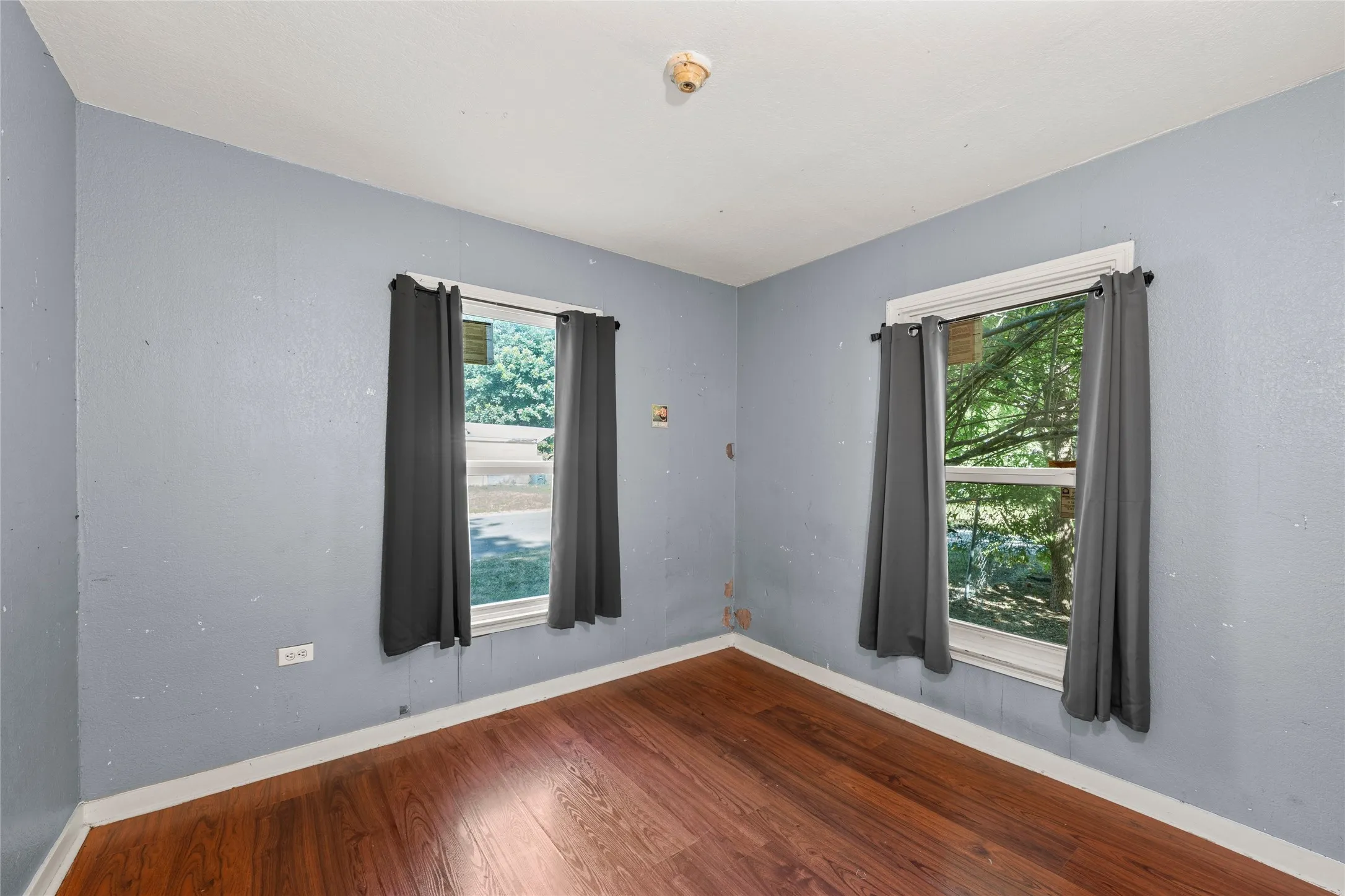 Interior room featuring wood-finish flooring, light blue wall paint, and two windows with white trim