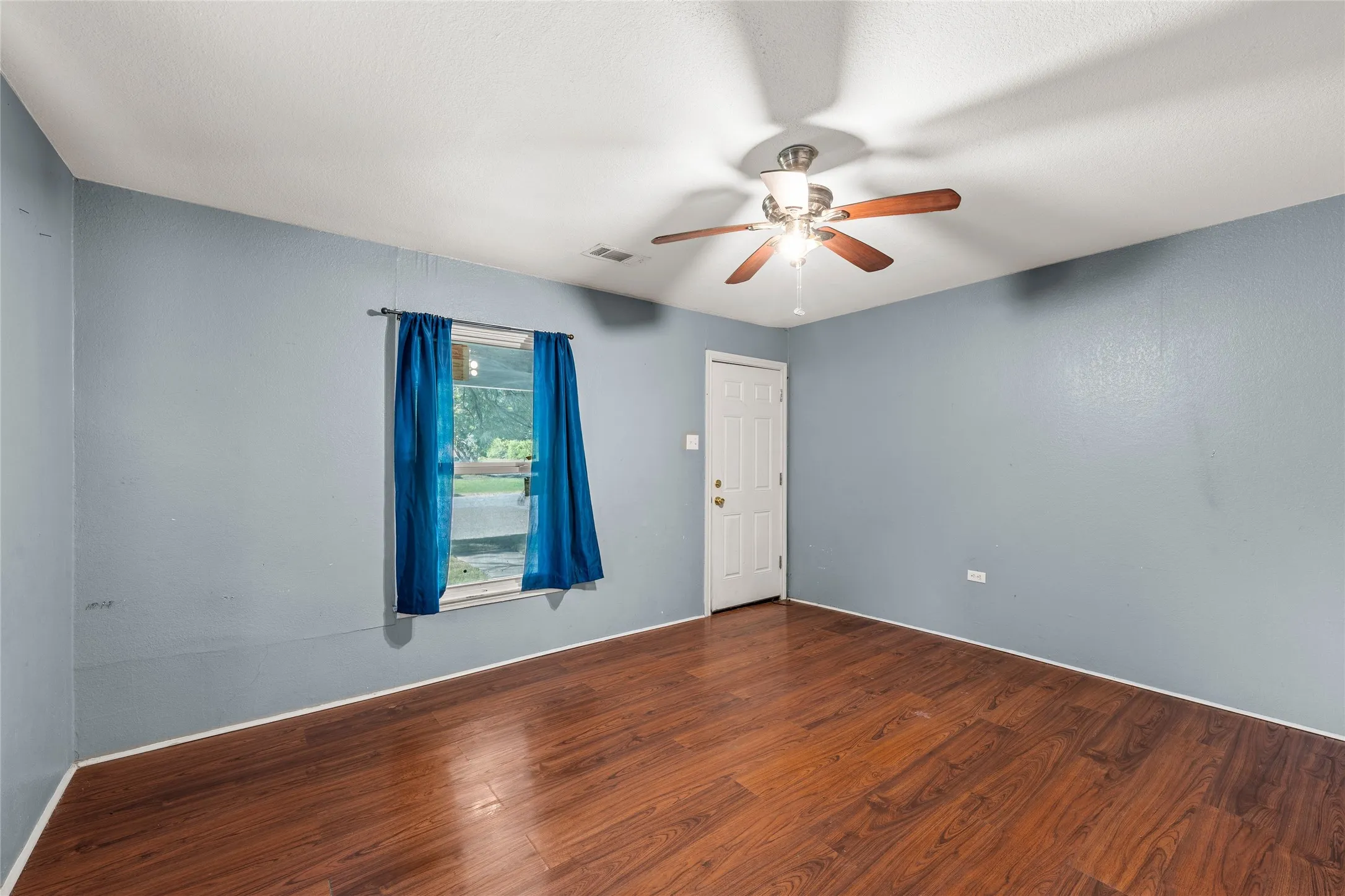 Interior room featuring wood-finish flooring, a ceiling fan with integrated lighting, a window, and a paneled door