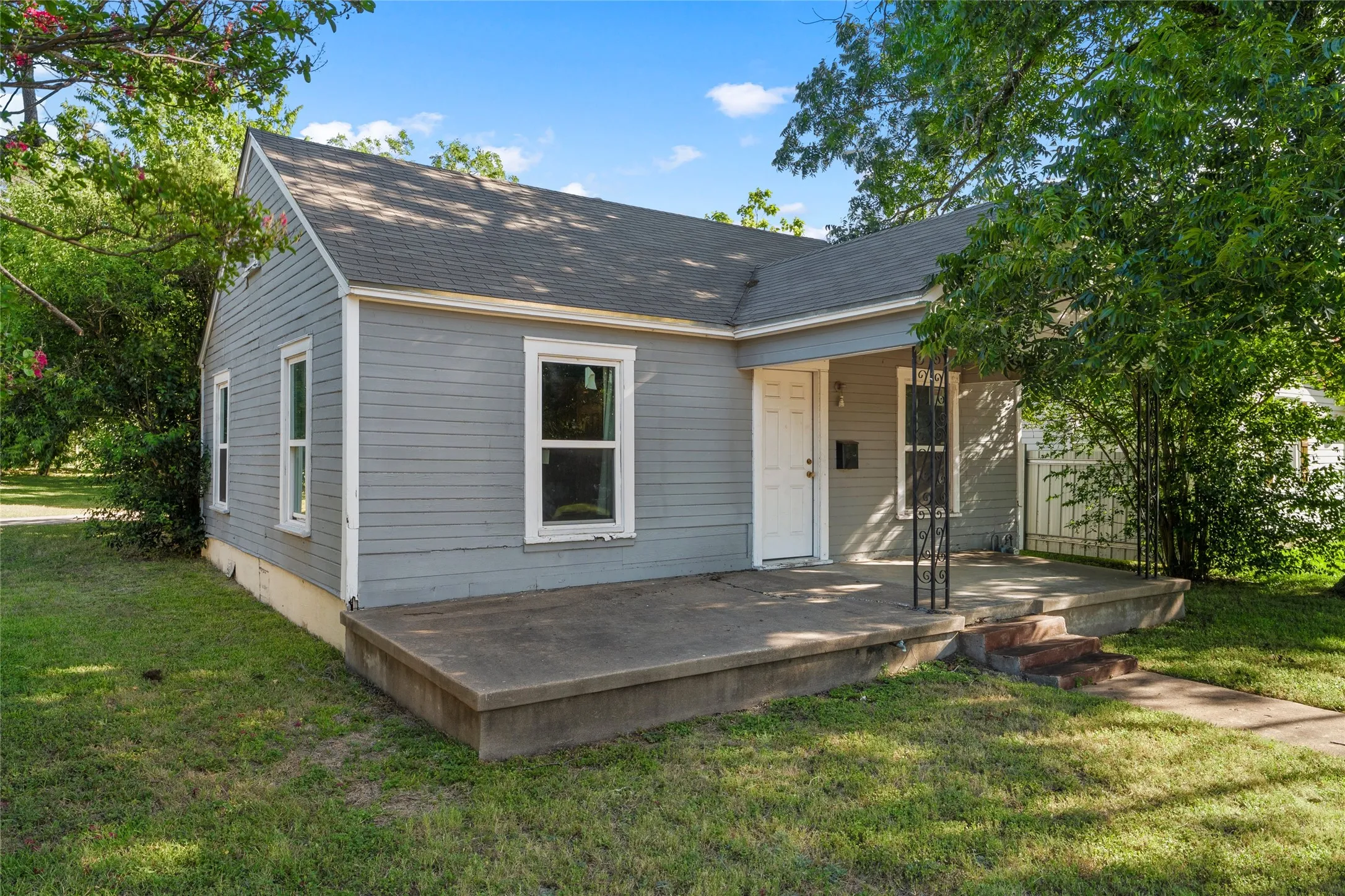 Gray siding residence featuring a concrete front porch, white entry door, and a gabled roofline