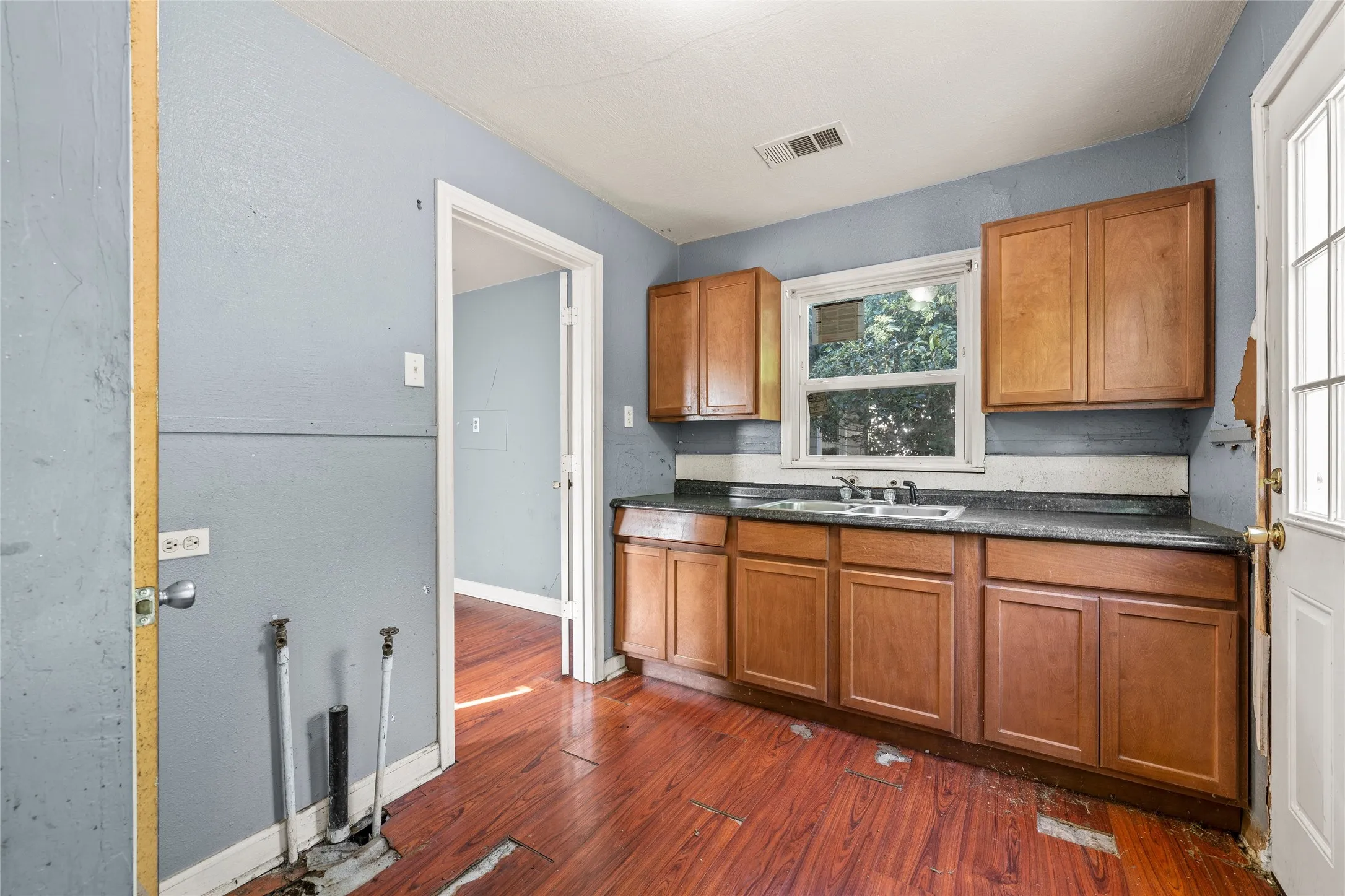 Kitchen featuring wood-finish flooring, wood cabinetry, a double-basin sink, a window, and a white exterior door