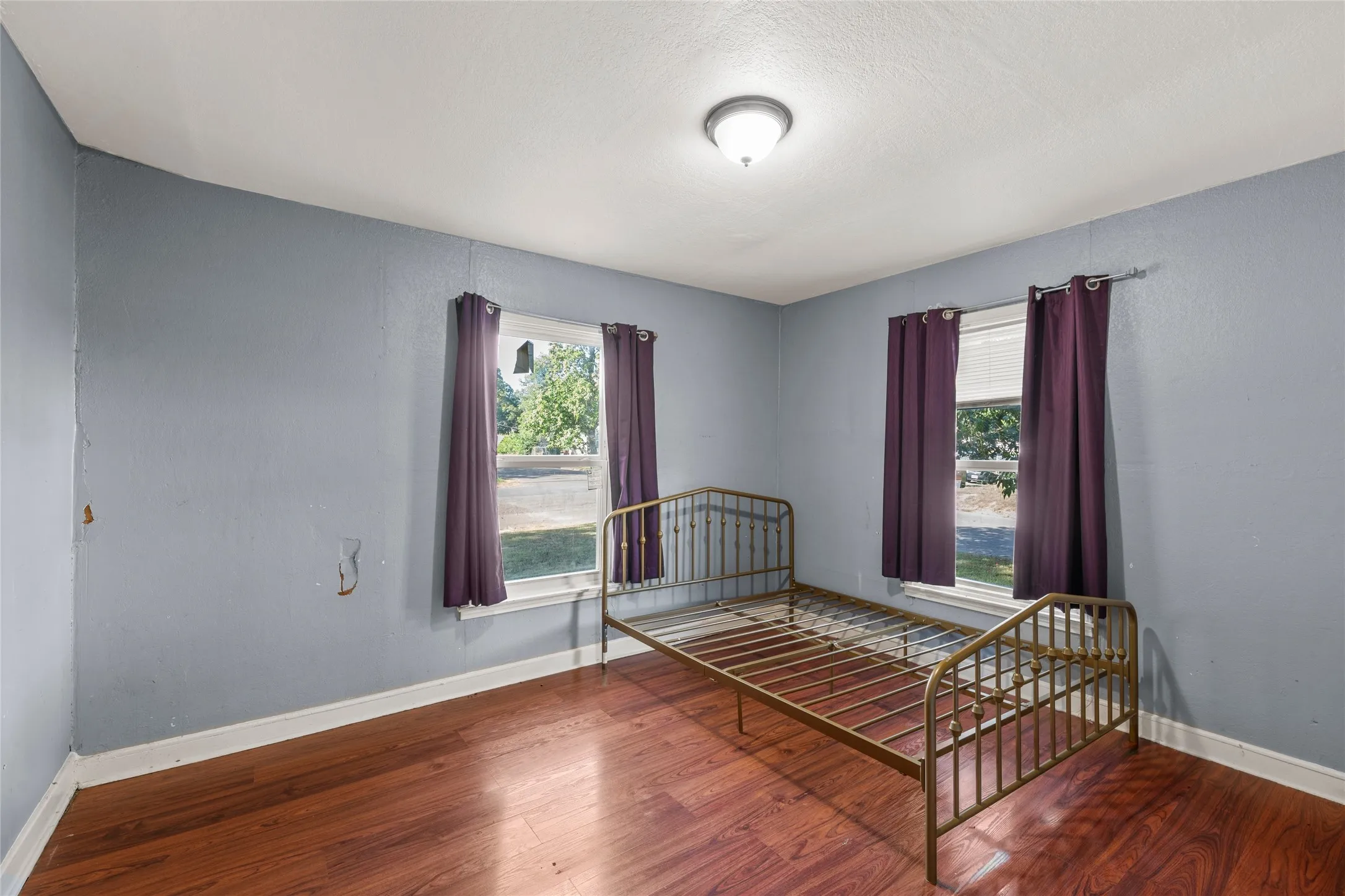 Bright room featuring two windows, wood-finish flooring, a ceiling-mounted light fixture, and light blue walls