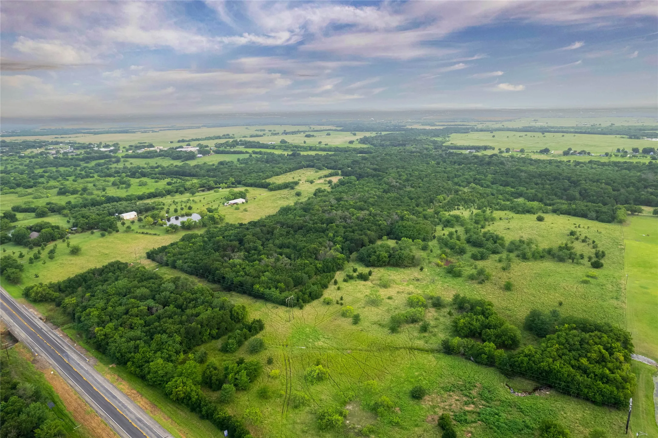 Expansive rural landscape featuring a mix of open grassy fields and dense tree clusters