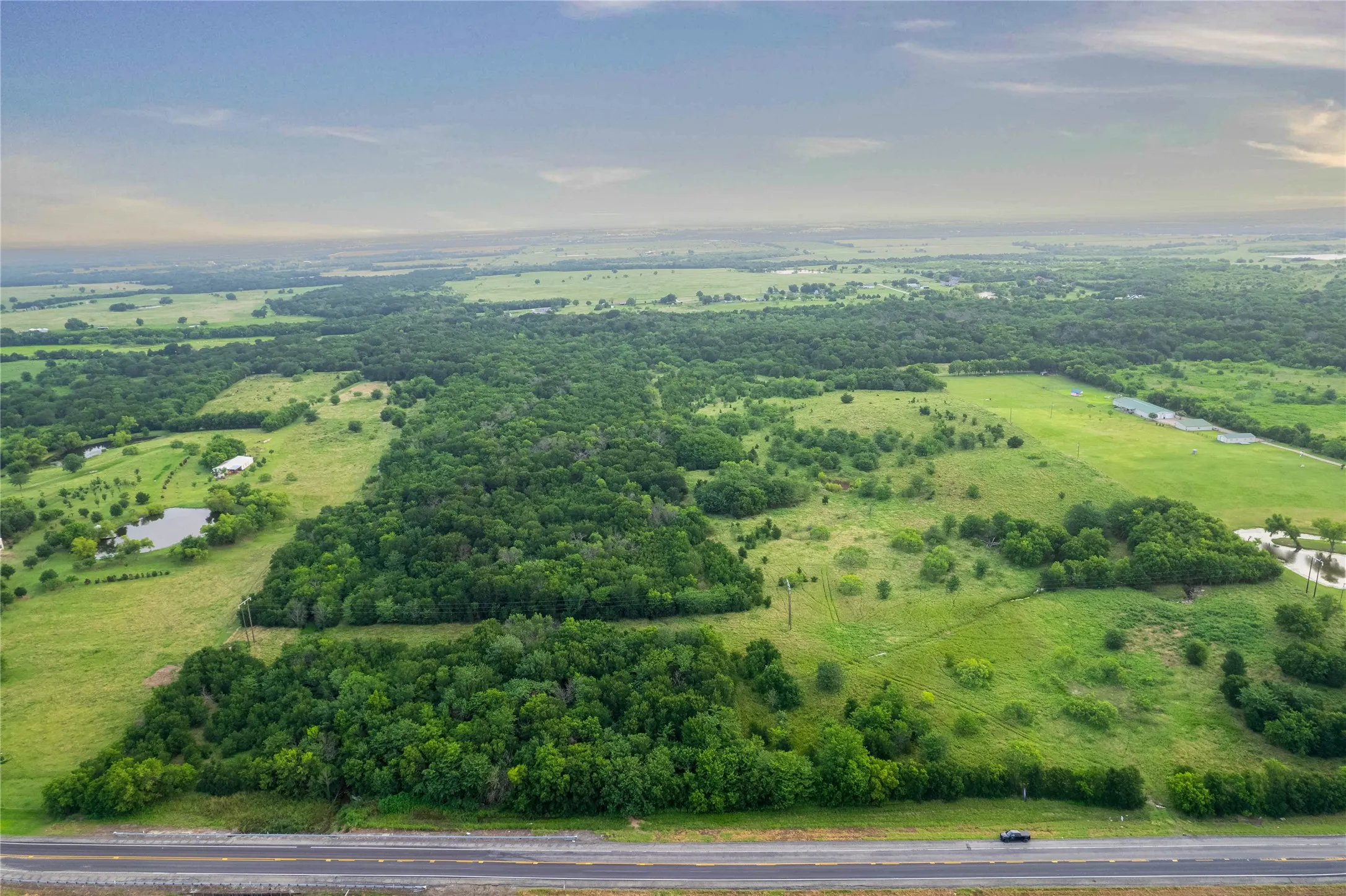 Expansive green landscape featuring mature tree lines, open fields, and two visible ponds