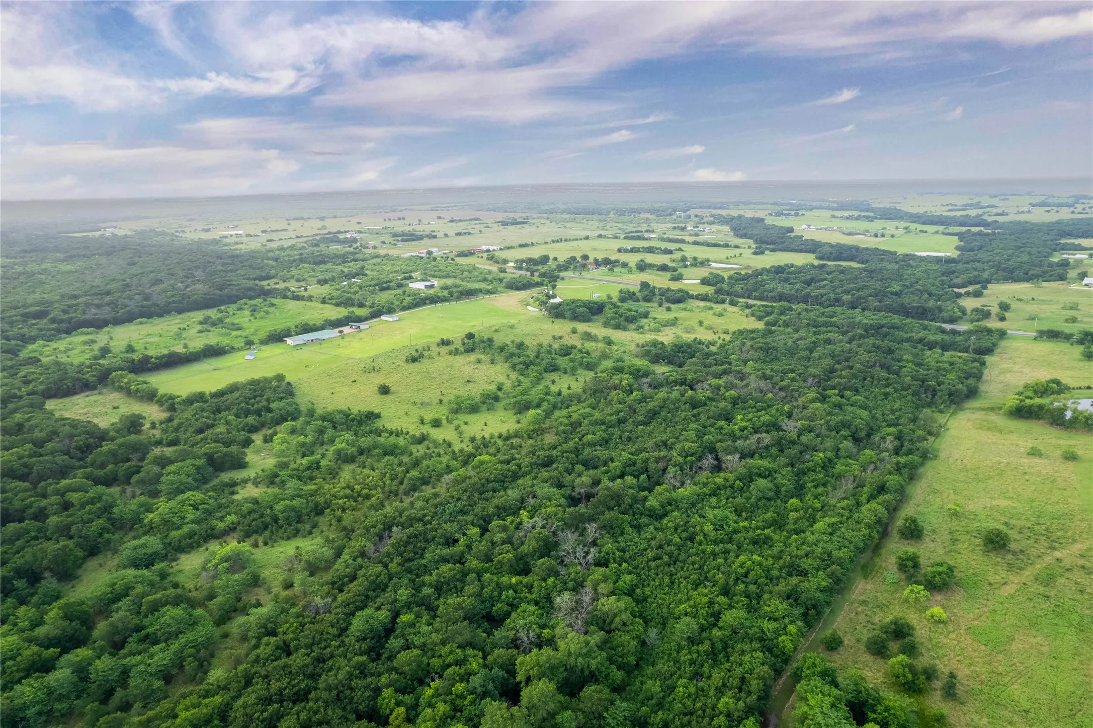 Expansive land parcel featuring a mix of dense wooded areas and open green fields