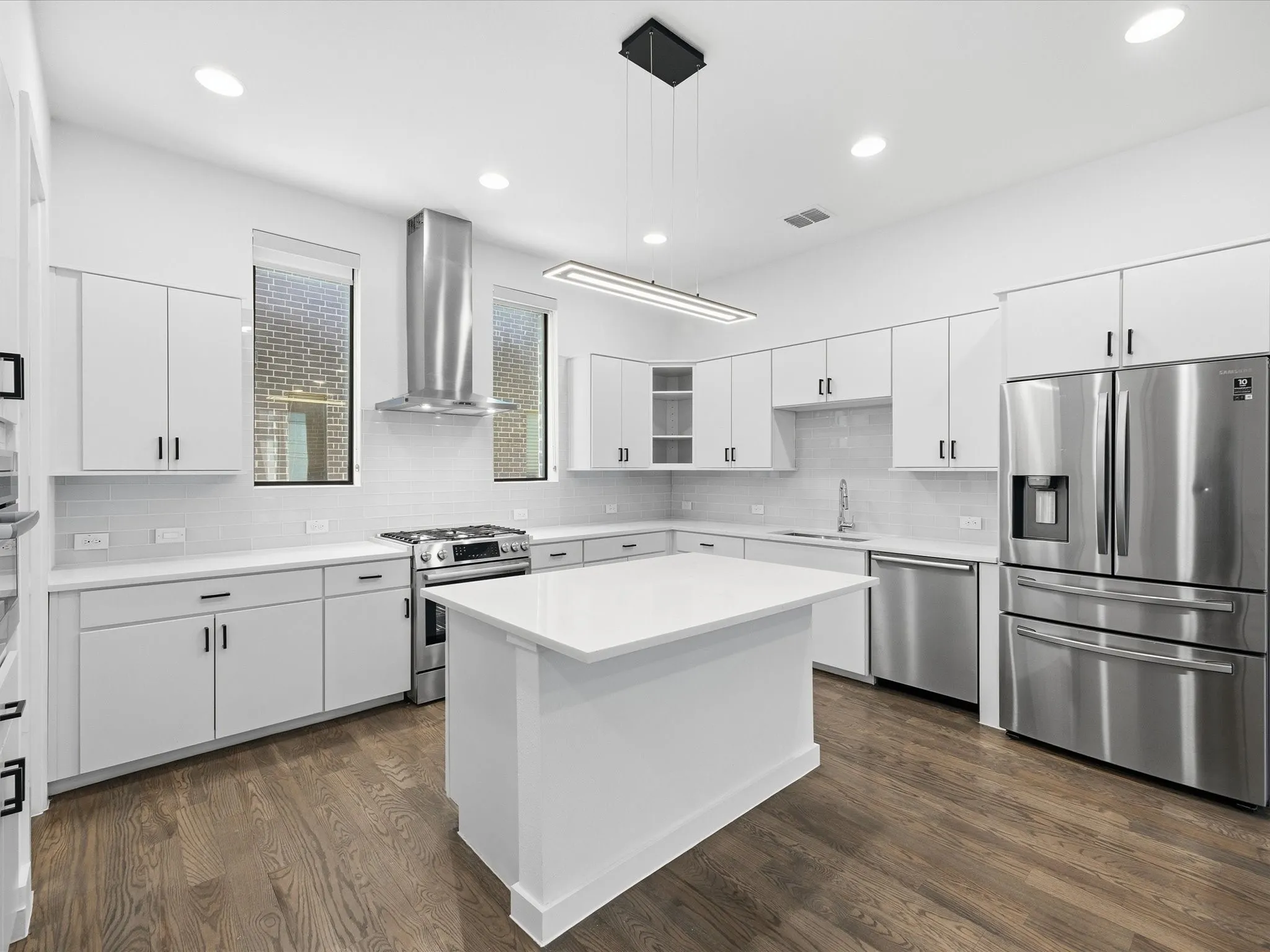 Kitchen with stainless steel appliances, white cabinets, dark wood-type flooring, decorative light fixtures, and glass insert cabinets