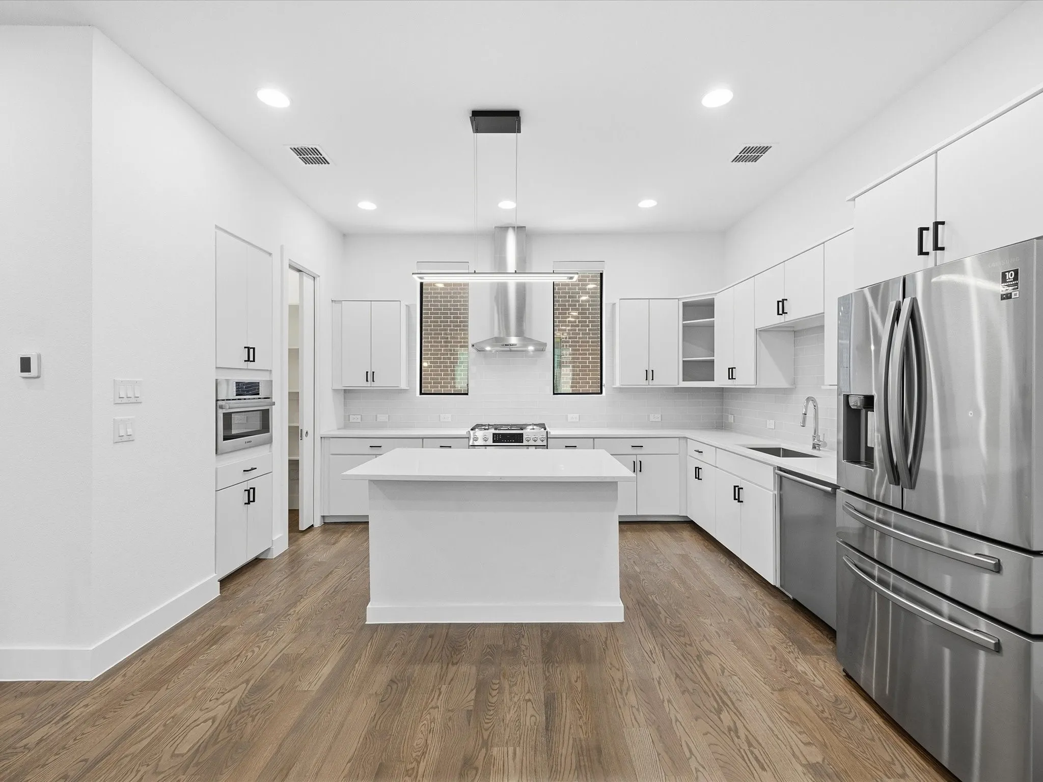 Kitchen with glass insert cabinets, stainless steel appliances, white cabinetry, and decorative light fixtures