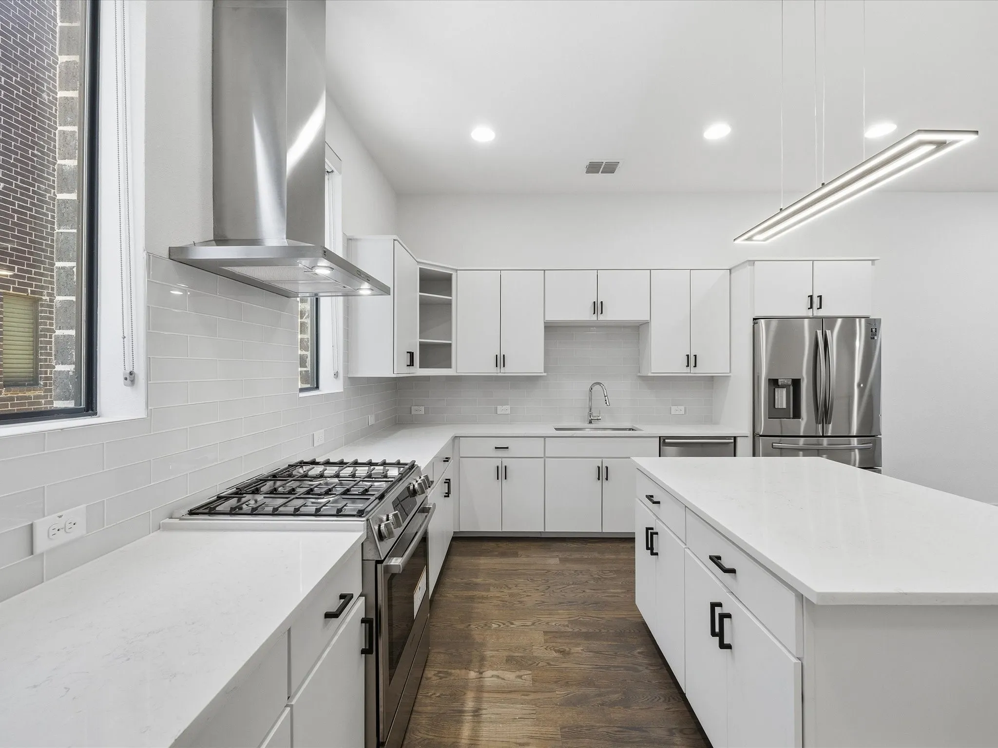 Kitchen with stainless steel appliances, range hood, dark wood-type flooring, white cabinets, and light stone counters