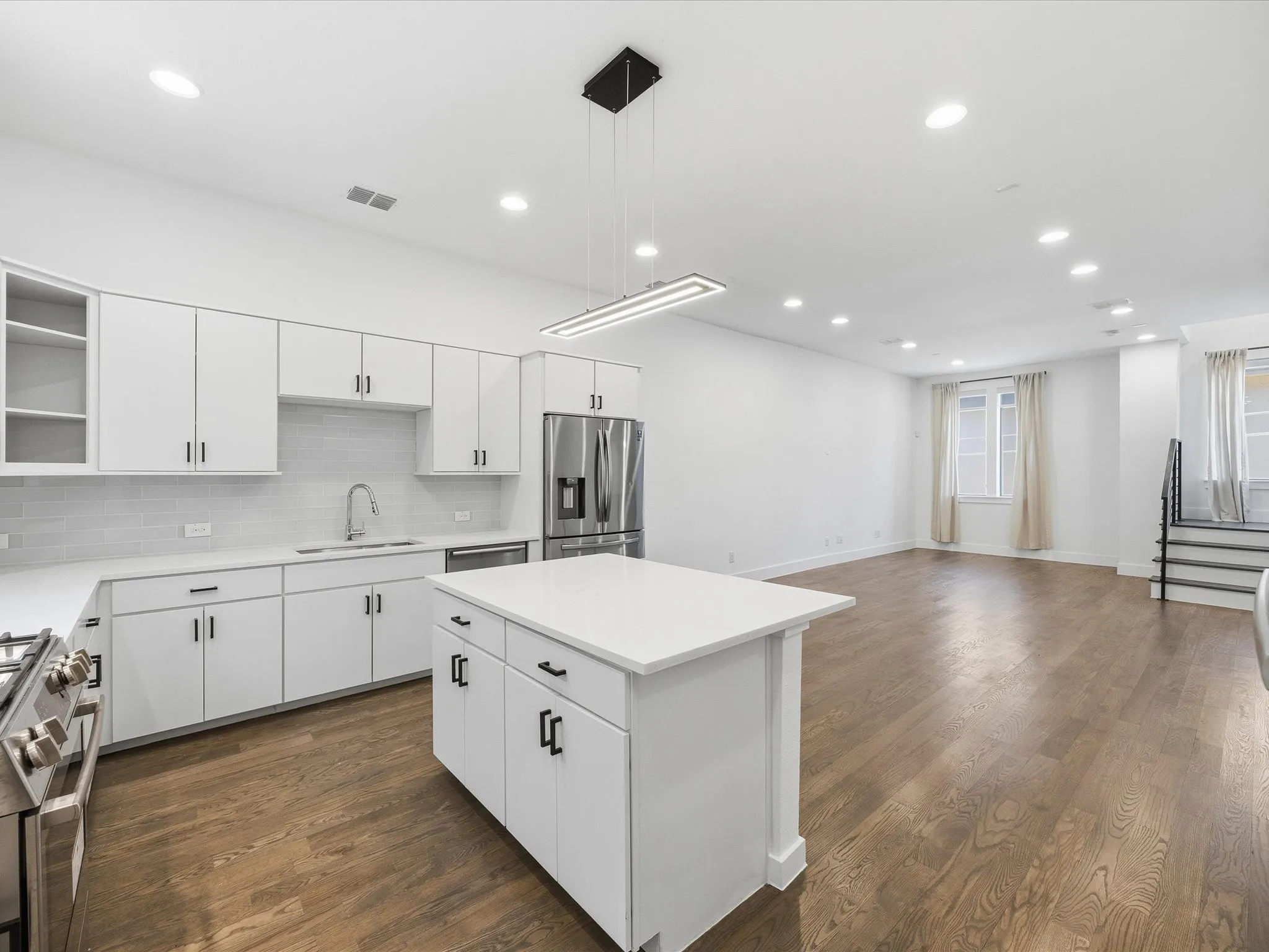 Kitchen with open floor plan, white cabinets, open shelves, stainless steel appliances, and pendant lighting