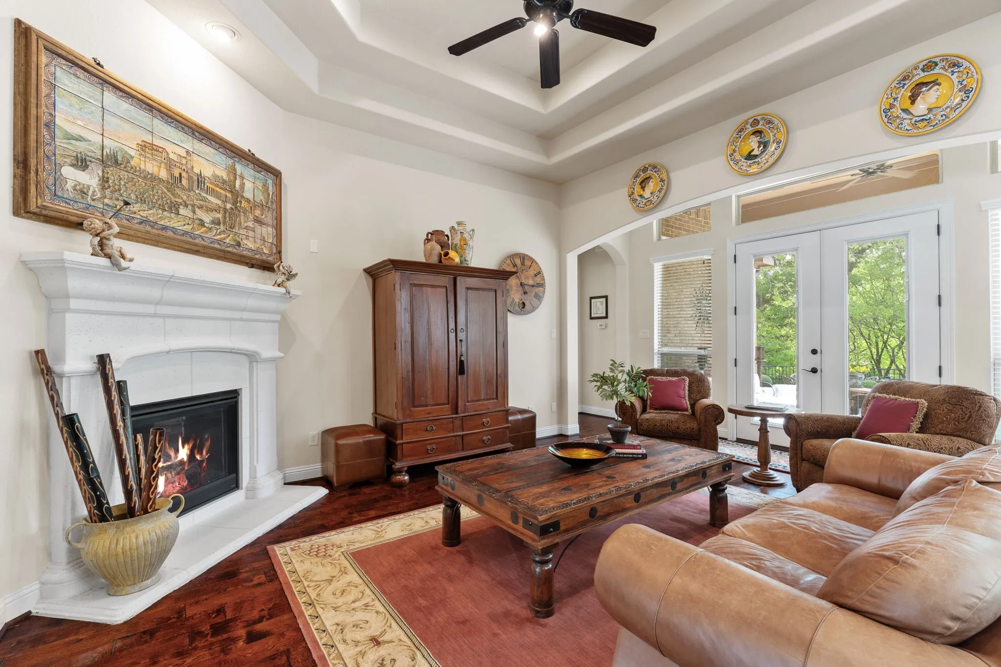 Living Room with hardwood flooring, trayed ceiling, window wall with French doors, gas fireplace, architectural details abound with arched doorways.