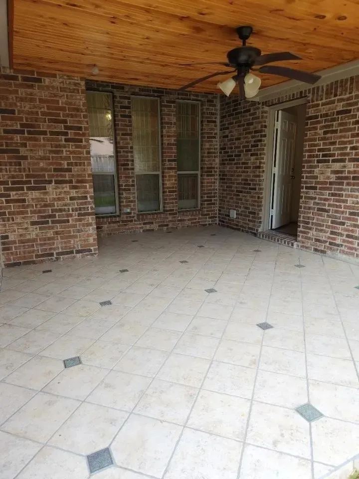 Covered patio featuring a wood-finish ceiling, ceiling fan with integrated lighting, brick exterior walls, and tiled flooring with decorative inlays
