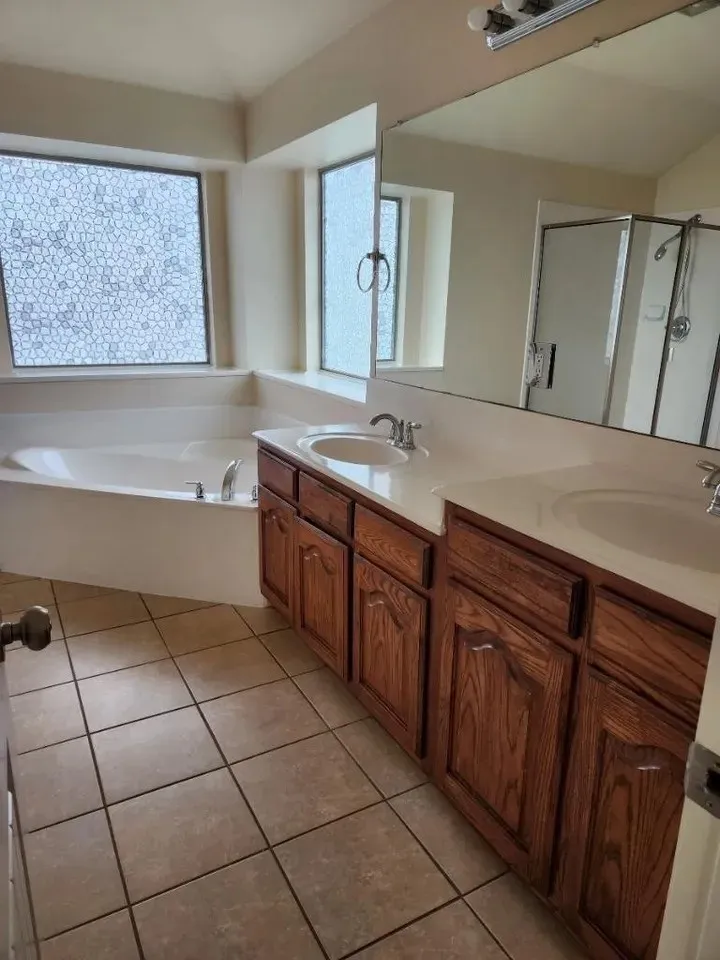 Bathroom featuring an integrated soaking tub, dual vanity with wood cabinetry, and a full-width mirror