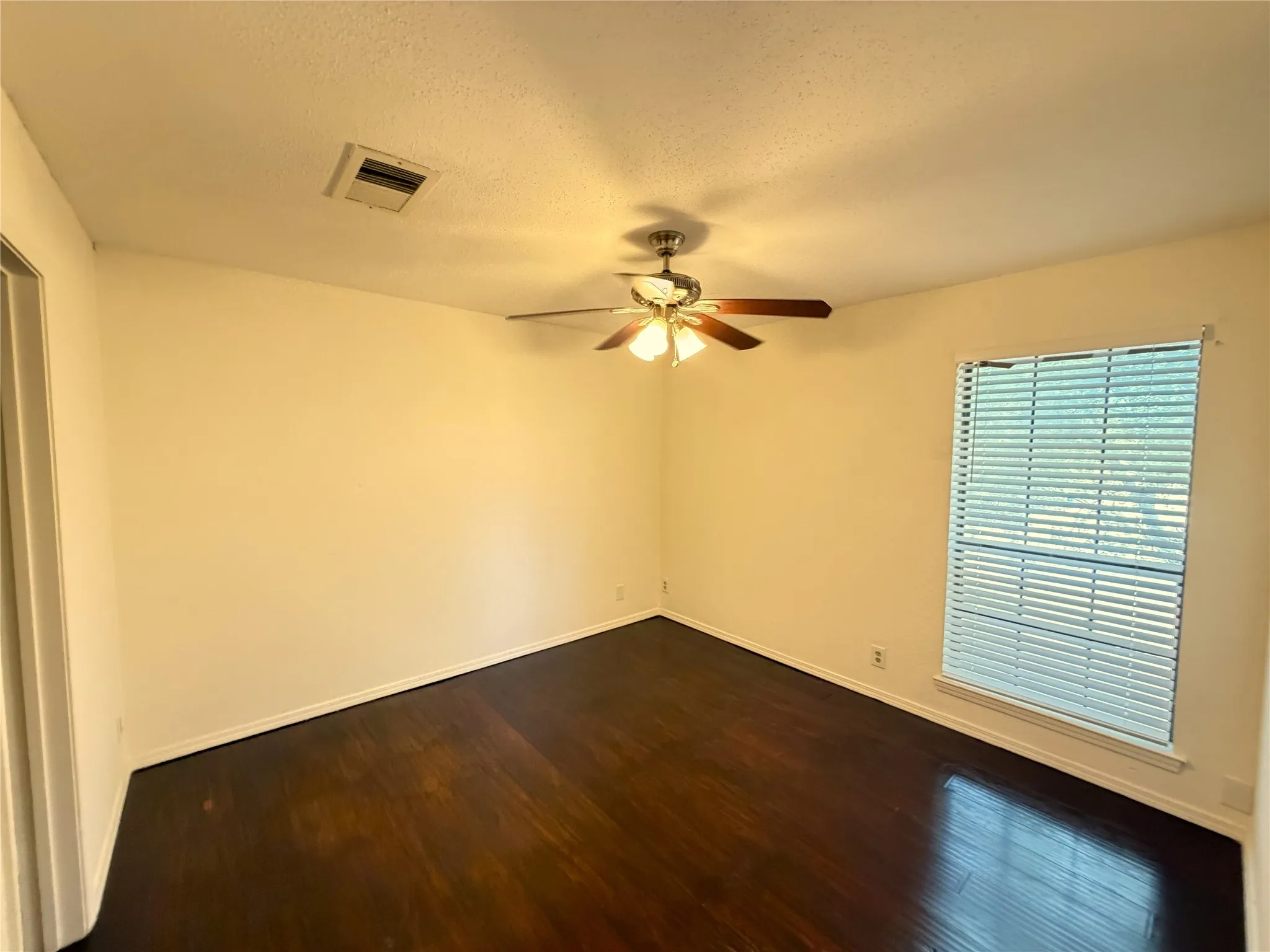 Spacious room featuring dark wood-finish flooring, light-toned walls, and a ceiling fan with integrated lighting