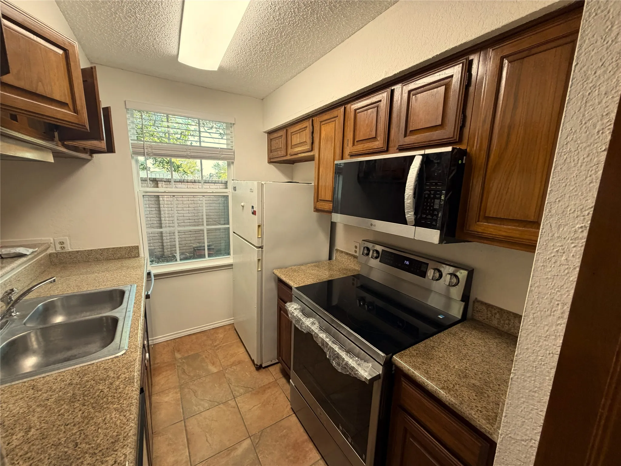 Kitchen featuring warm wood cabinetry, neutral countertops, a double basin stainless steel sink, a stainless steel electric range, and an over-the-range microwave