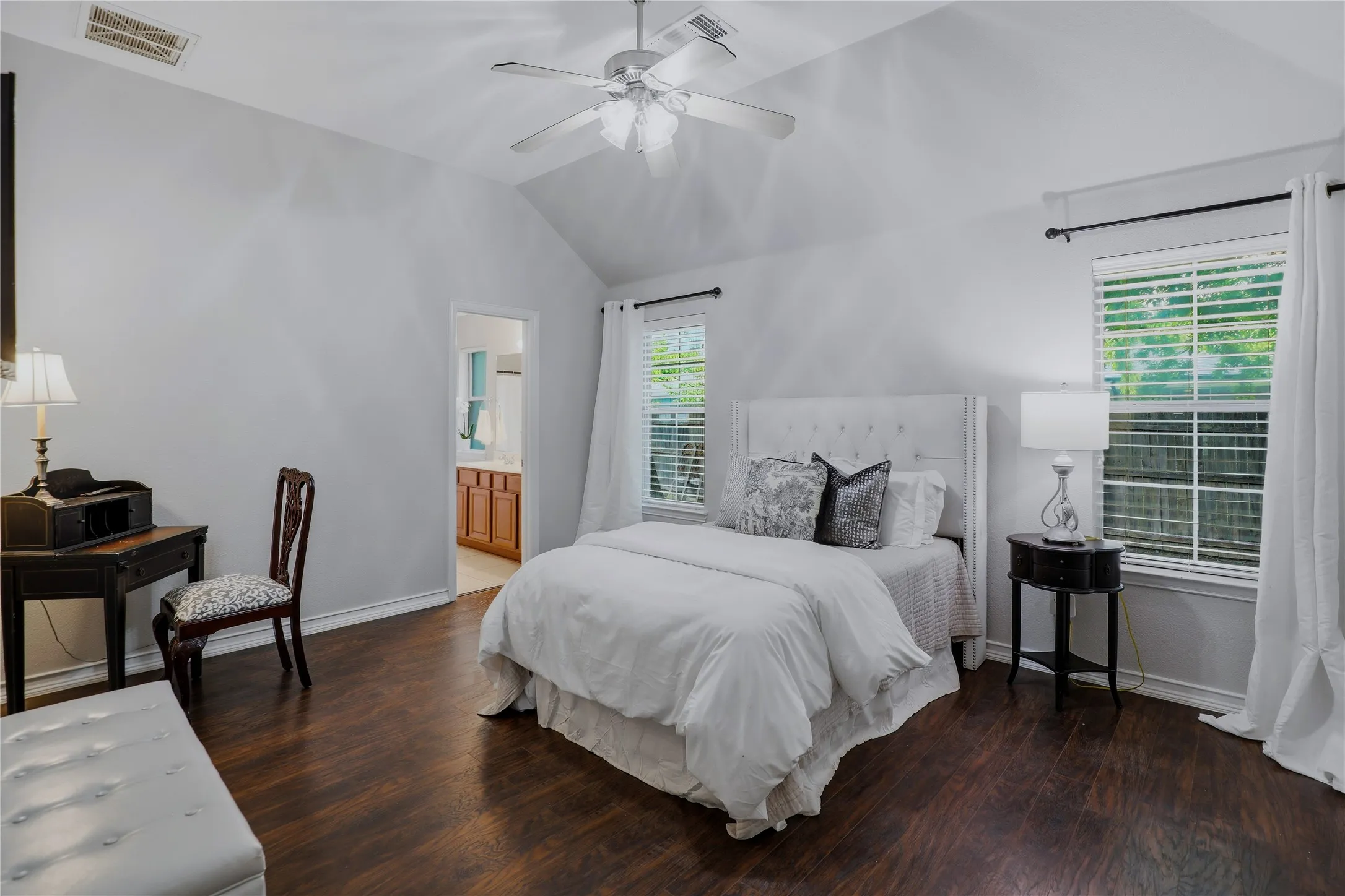 Spacious bedroom featuring vaulted ceilings, rich wood-finish flooring, two large windows with blinds, and a ceiling fan
