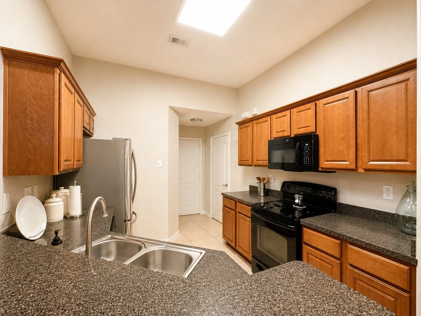 Functional kitchen featuring warm wood cabinetry, dark speckled countertops, a double basin stainless steel sink, and black appliances