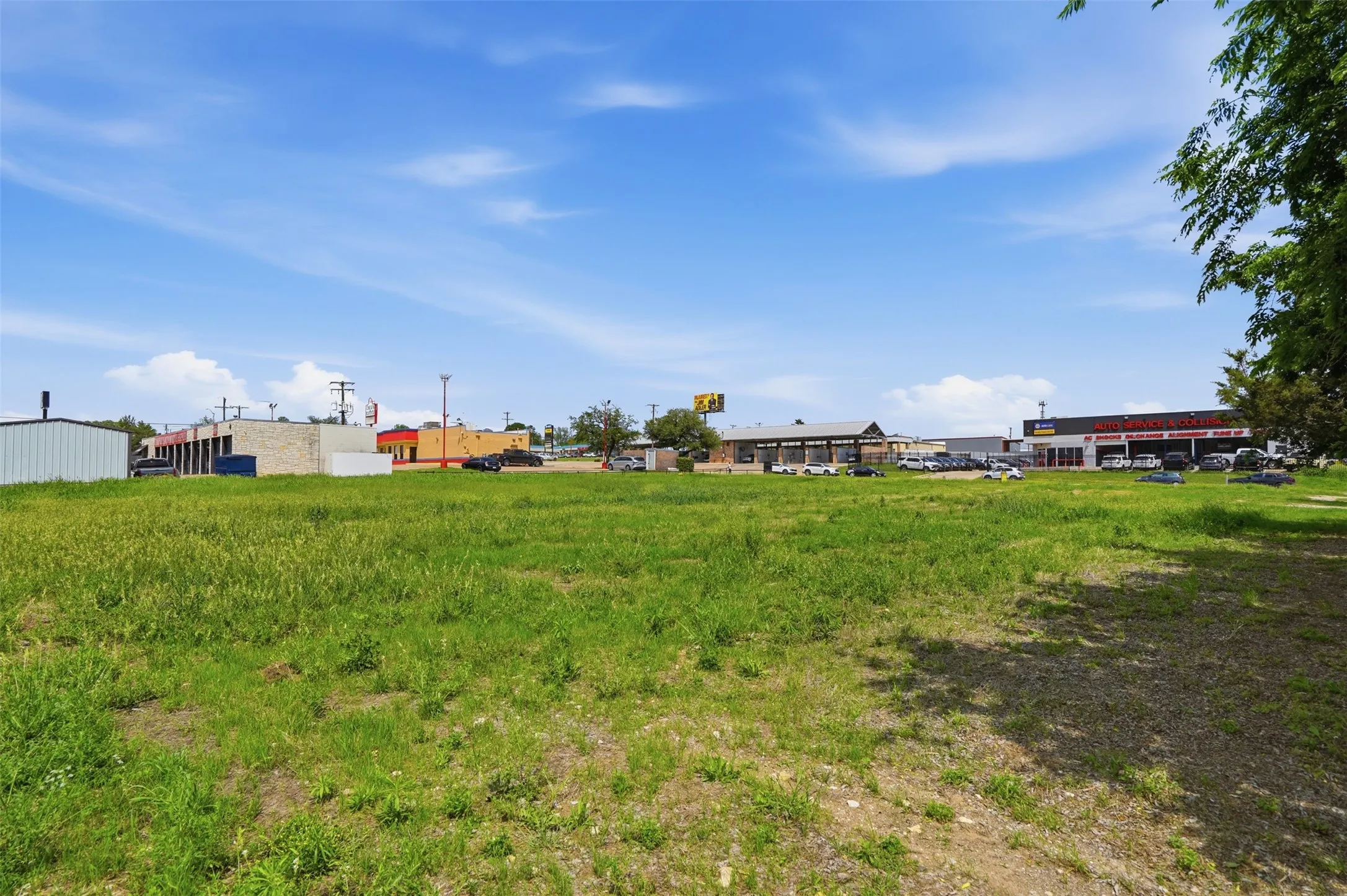 Expansive undeveloped lot featuring natural ground cover, surrounded by commercial establishments