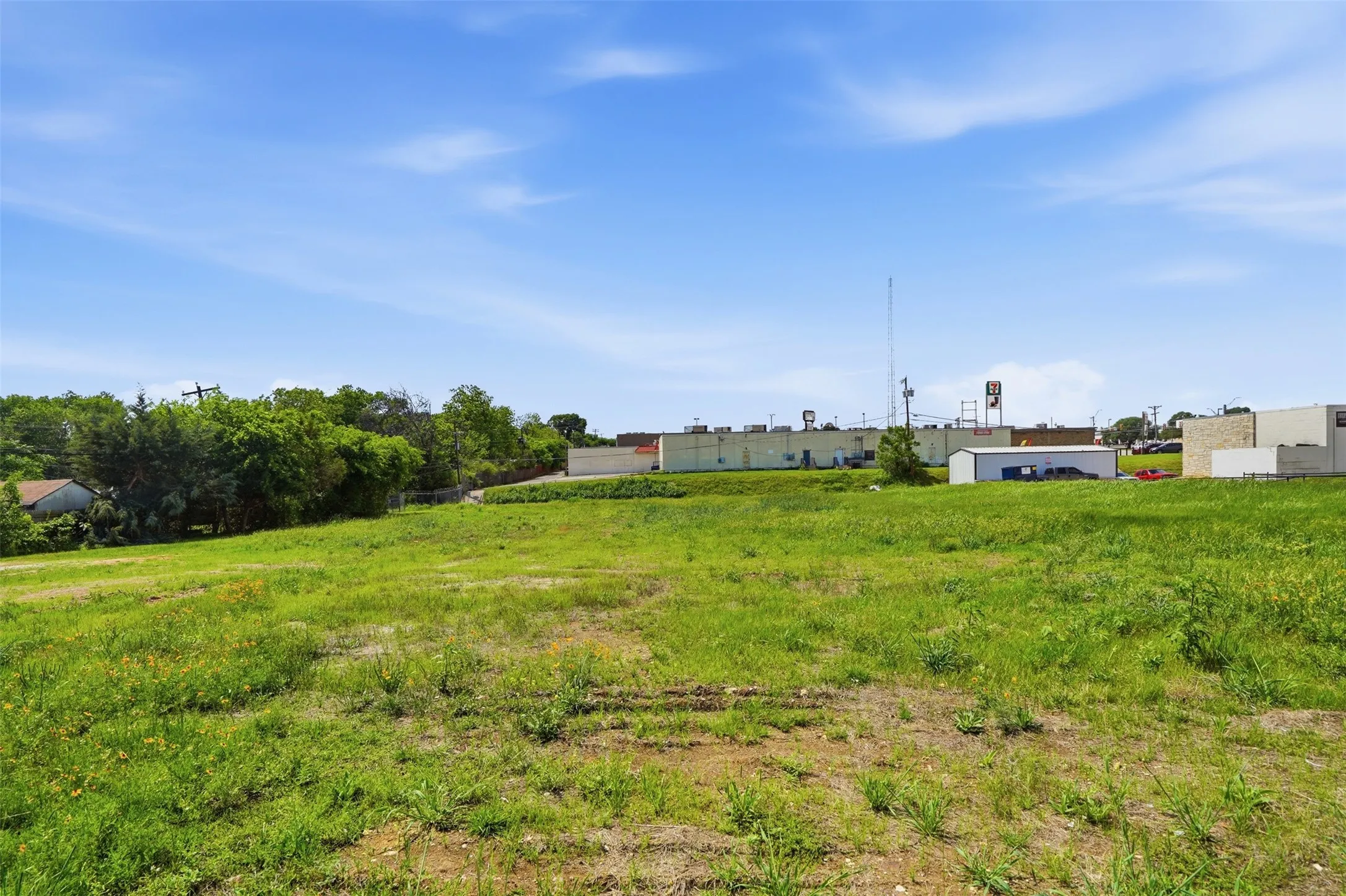 Expansive grassy lot featuring varied terrain and partial tree coverage